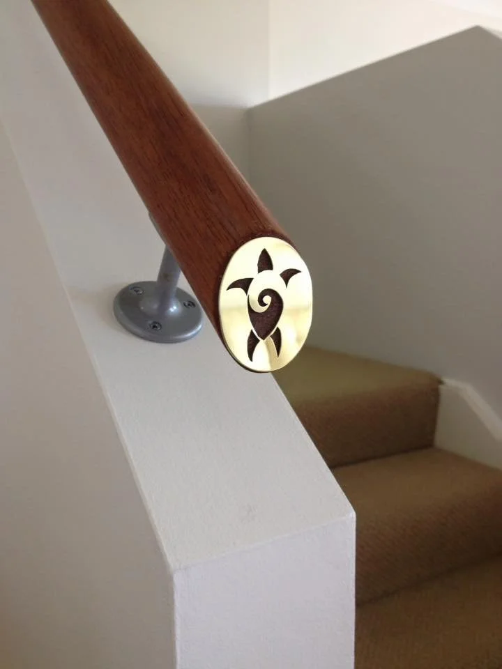 A close-up of a staircase railing with a decorative end cap featuring a turtle design made of wood and metal.