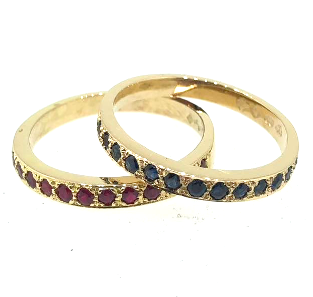 Two gold rings with colored gemstones, one with pink stones and the other with blue stones.
