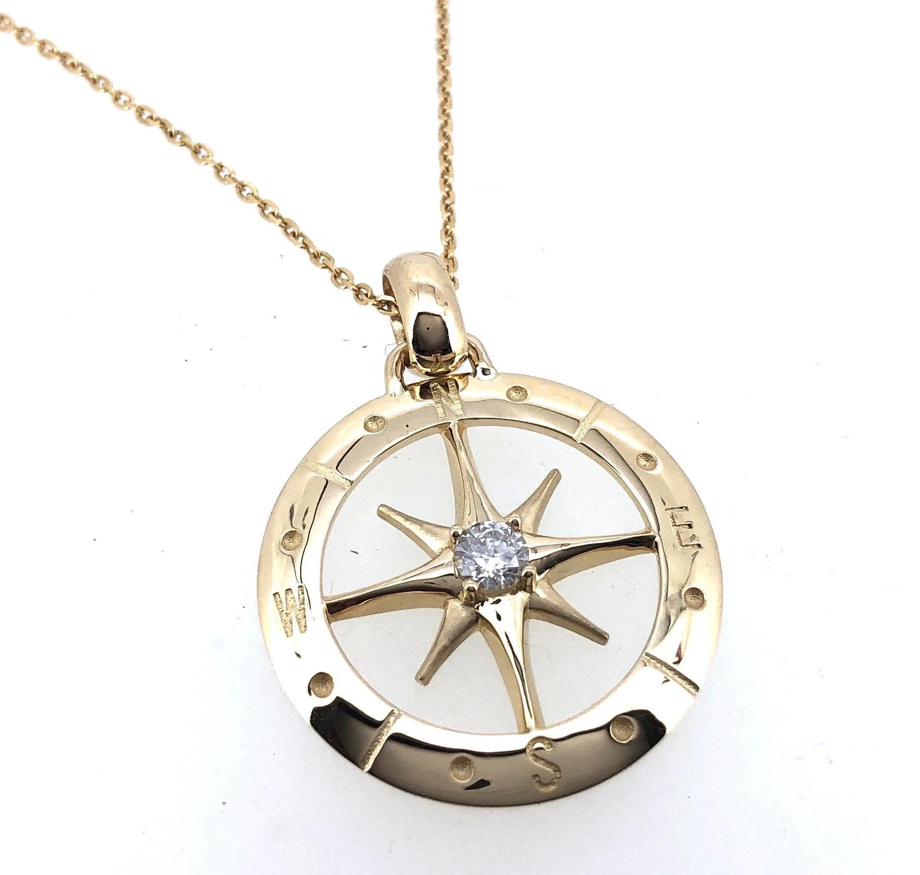 Gold necklace with a round pendant featuring a star and a diamond at the center, designed to resemble a compass. 