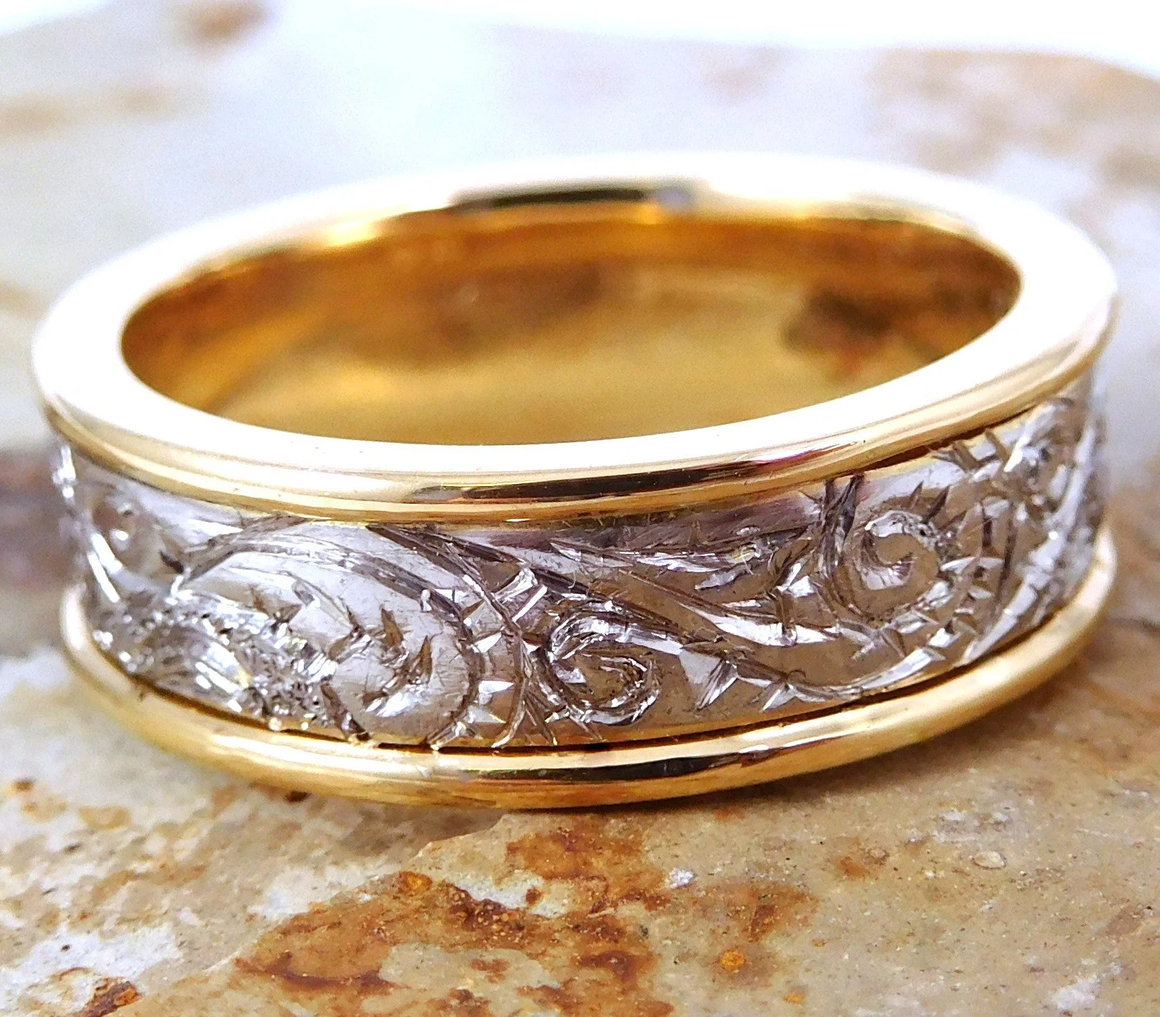 Close-up of a decorative ring with a gold-colored interior and an ornate silver exterior, placed on a textured surface.
