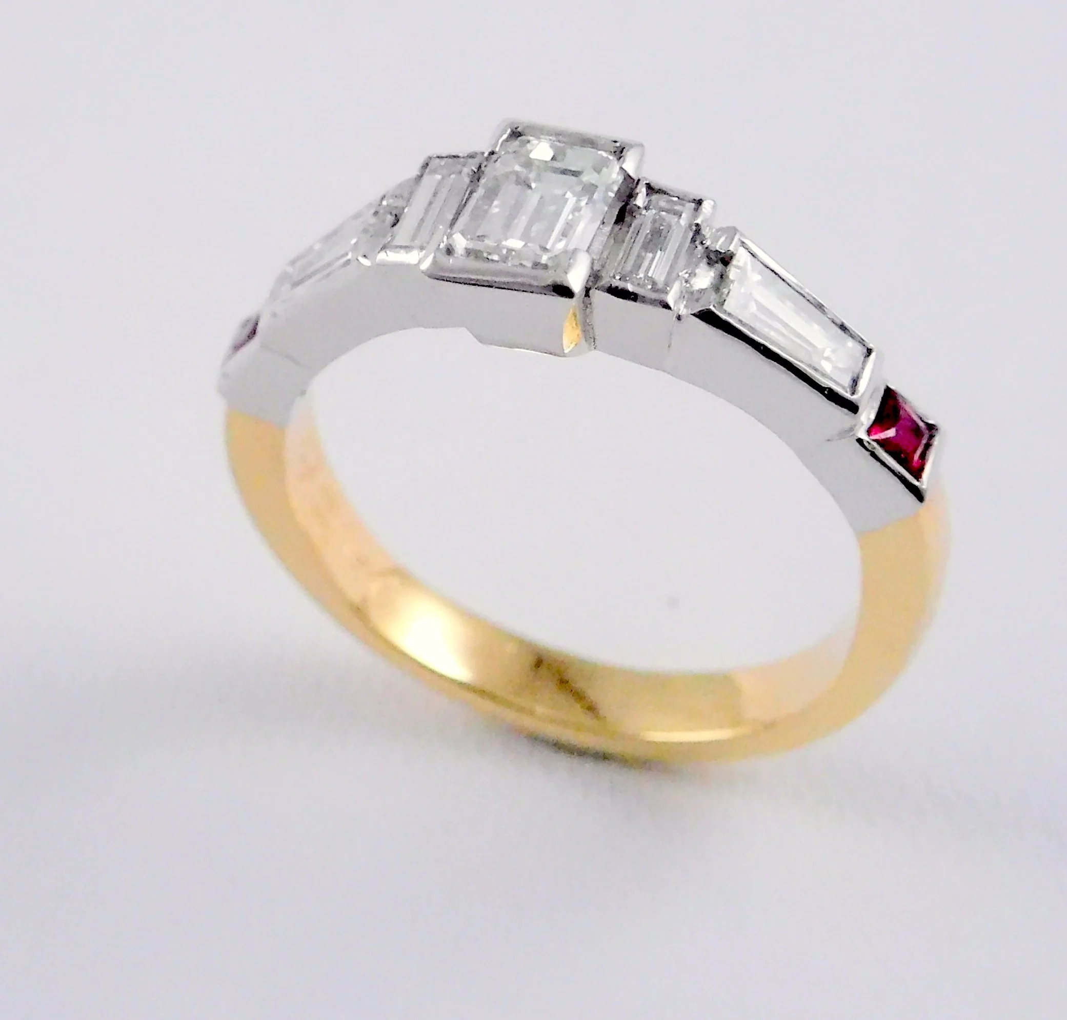 Close-up of a silver ring featuring a central emerald-cut diamond flanked by two emerald-cut diamonds on each side with a white background.