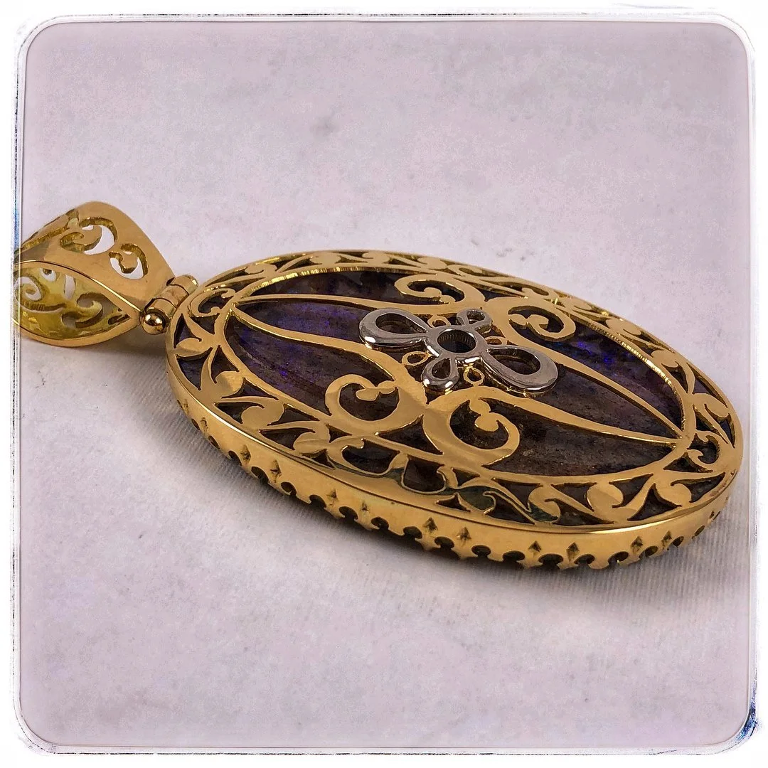 The back side of a gold oval pendant with intricate openwork design and a dark gemstone in the center.