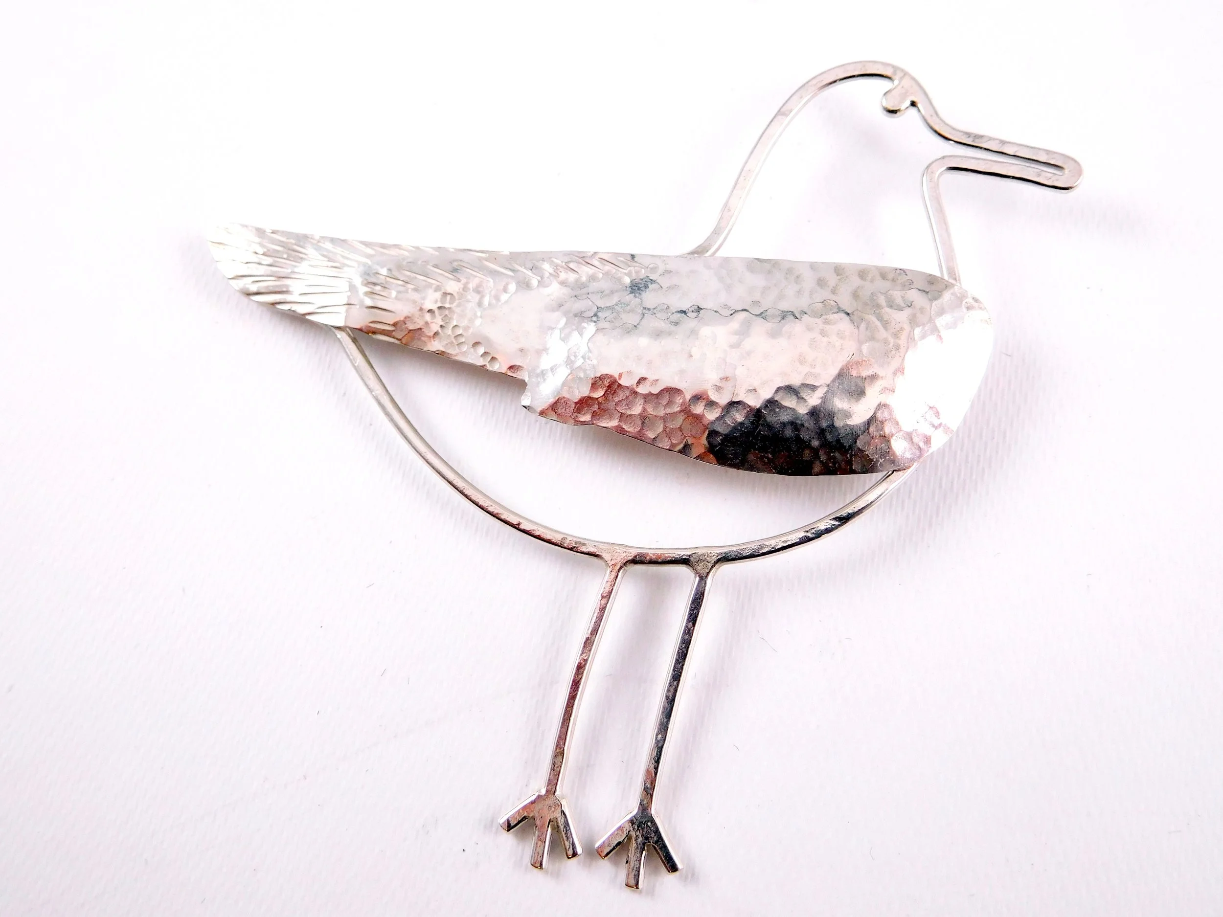 A decorative silver seagull brooch with hammered texture. 