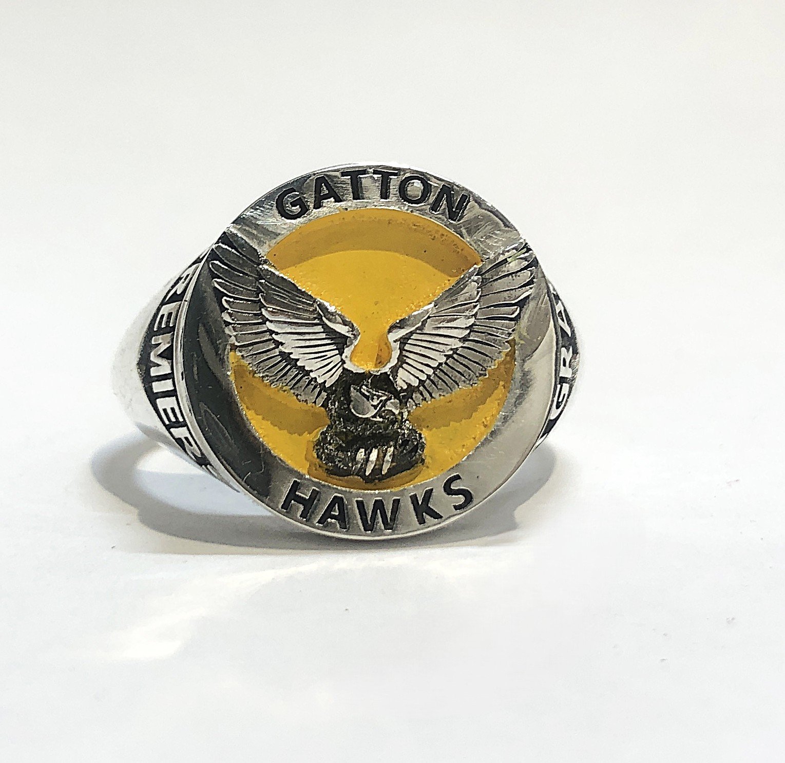 A silver ring with a yellow background featuring a black and white hawk with outstretched wings. The ring has the words "GATTAN HAWKS" inscribed around the top and bottom edges.