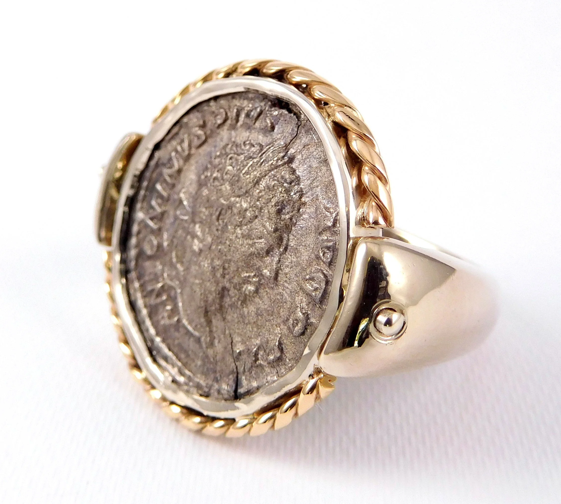 Close-up photo of a vintage coin ring with a two-tone gold braided band, placed on a white surface.