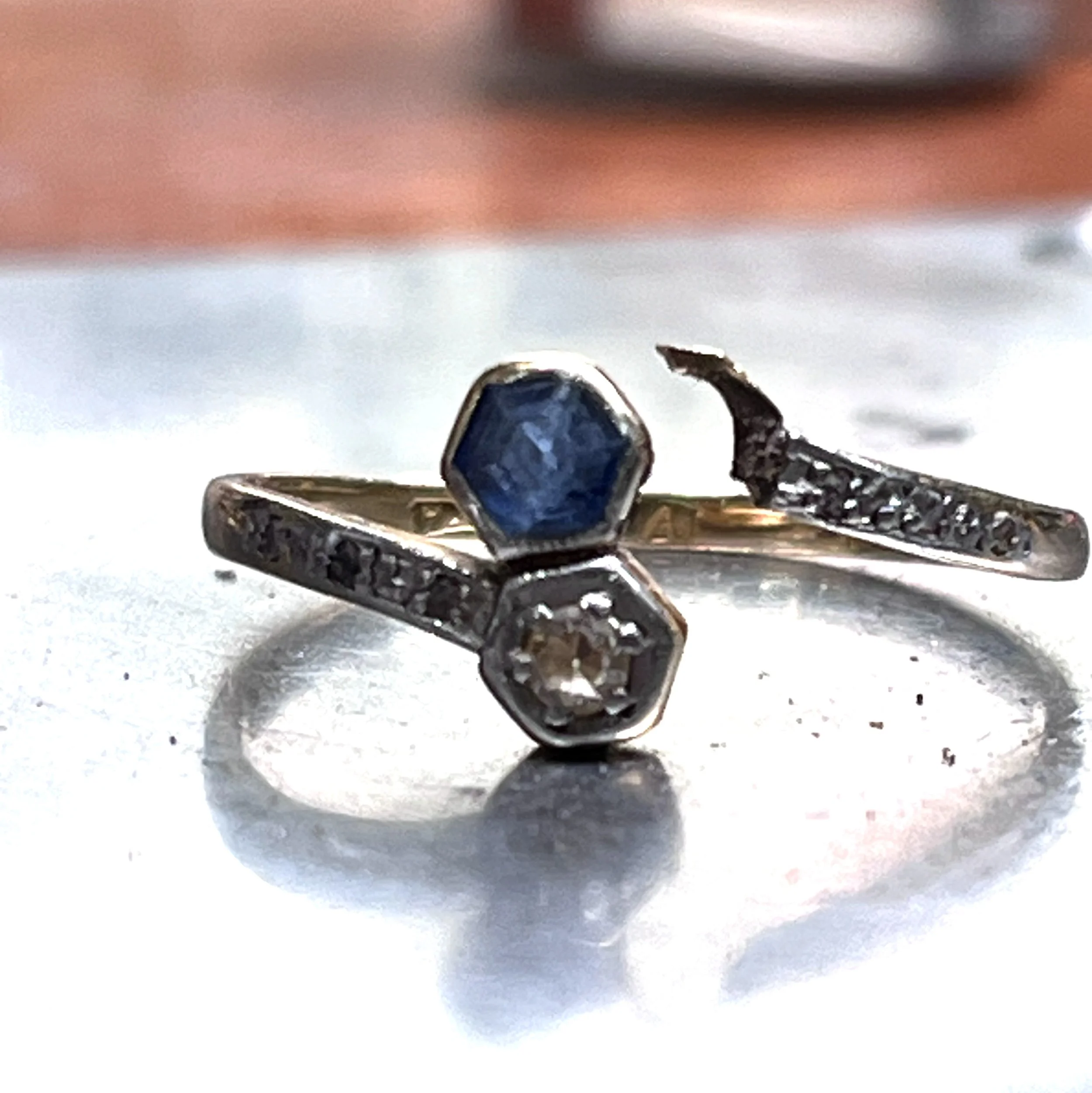 Close-up of a ring with a large blue gemstone set in a silver band, with a small insect on the band, placed on a white surface.