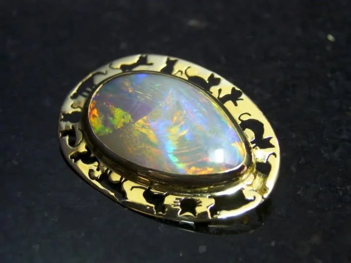 A gold ring with carved cat detailing and an oval-shaped opal gemstone reflecting rainbow colors