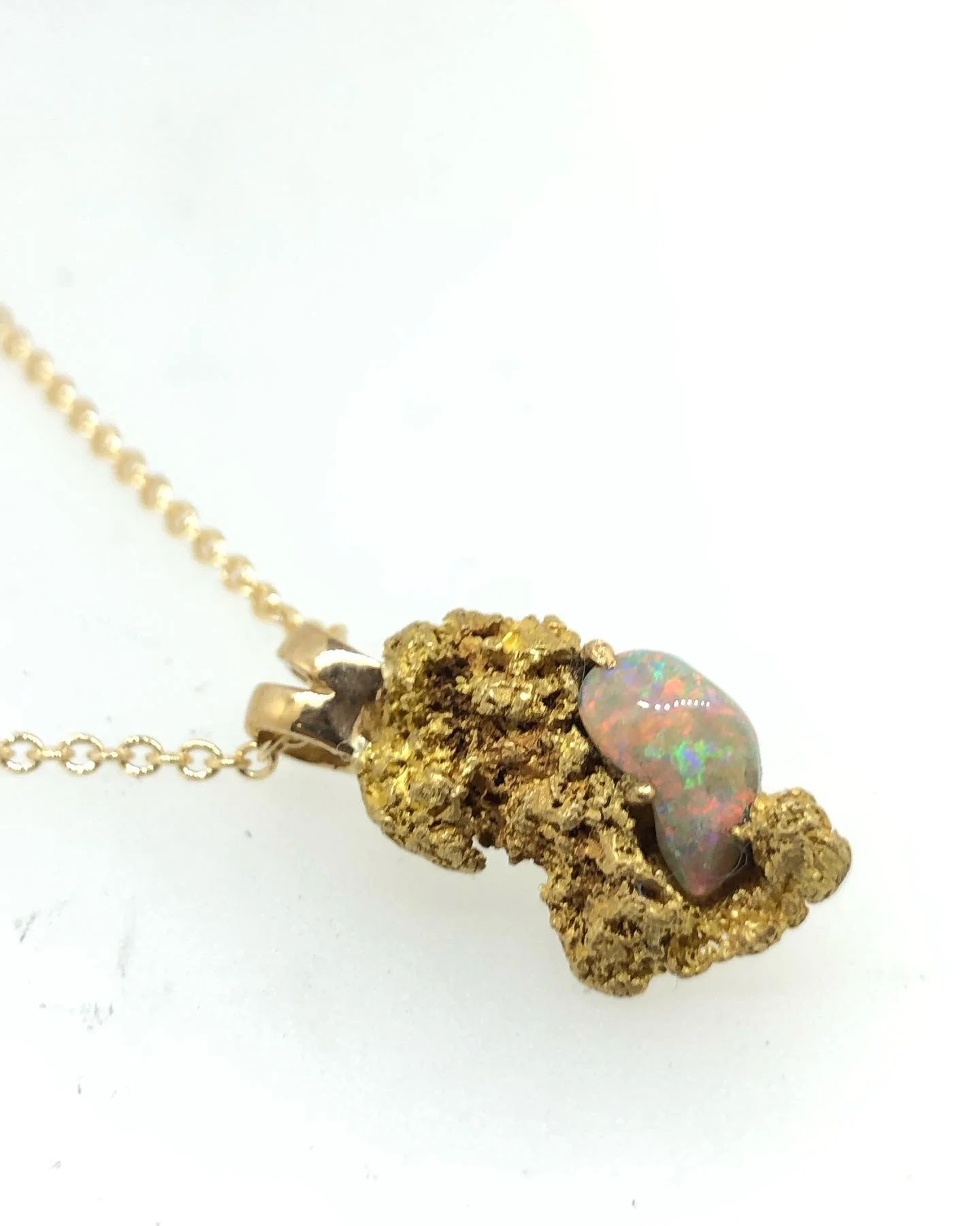 A gold necklace with a pendant made of a solid gold nuggest and a small opal stone.