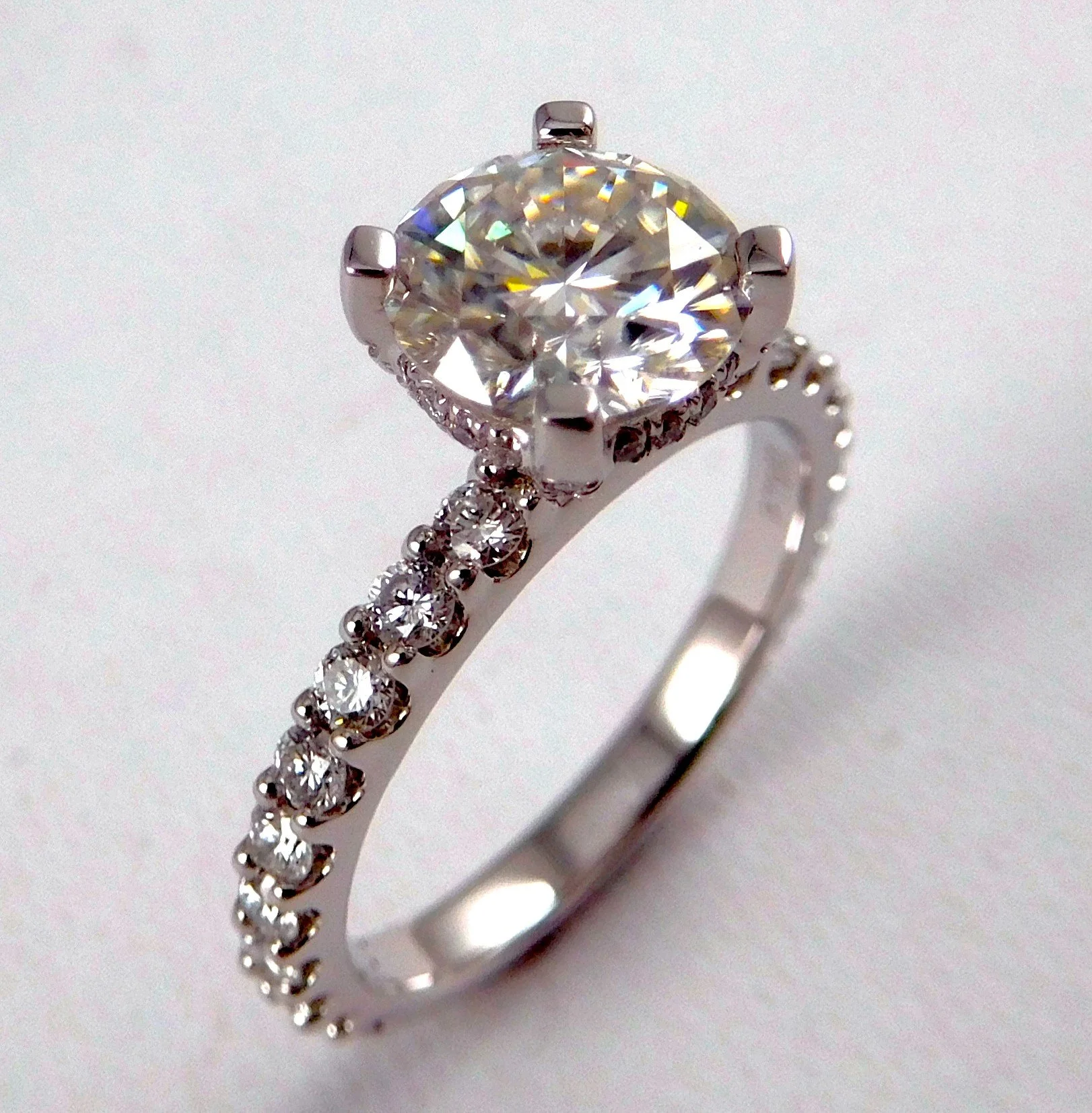 A silver ring with a large round diamond at the center, surrounded by smaller diamonds, is placed on a white surface.