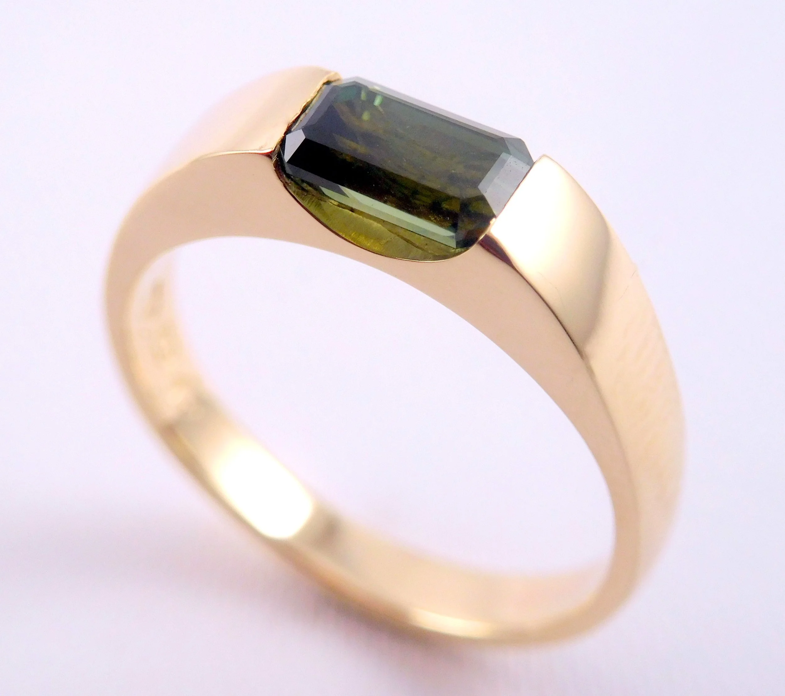 Close-up of a gold ring with a large, rectangular black gemstone on a white background.