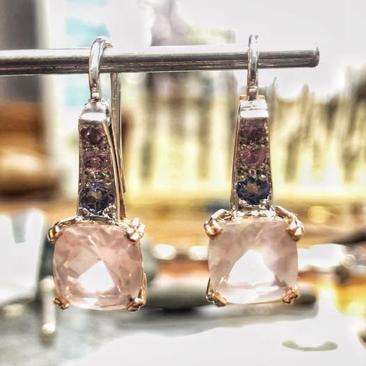 Pair of white gold earrings with large pink gemstones hanging on a display stand.