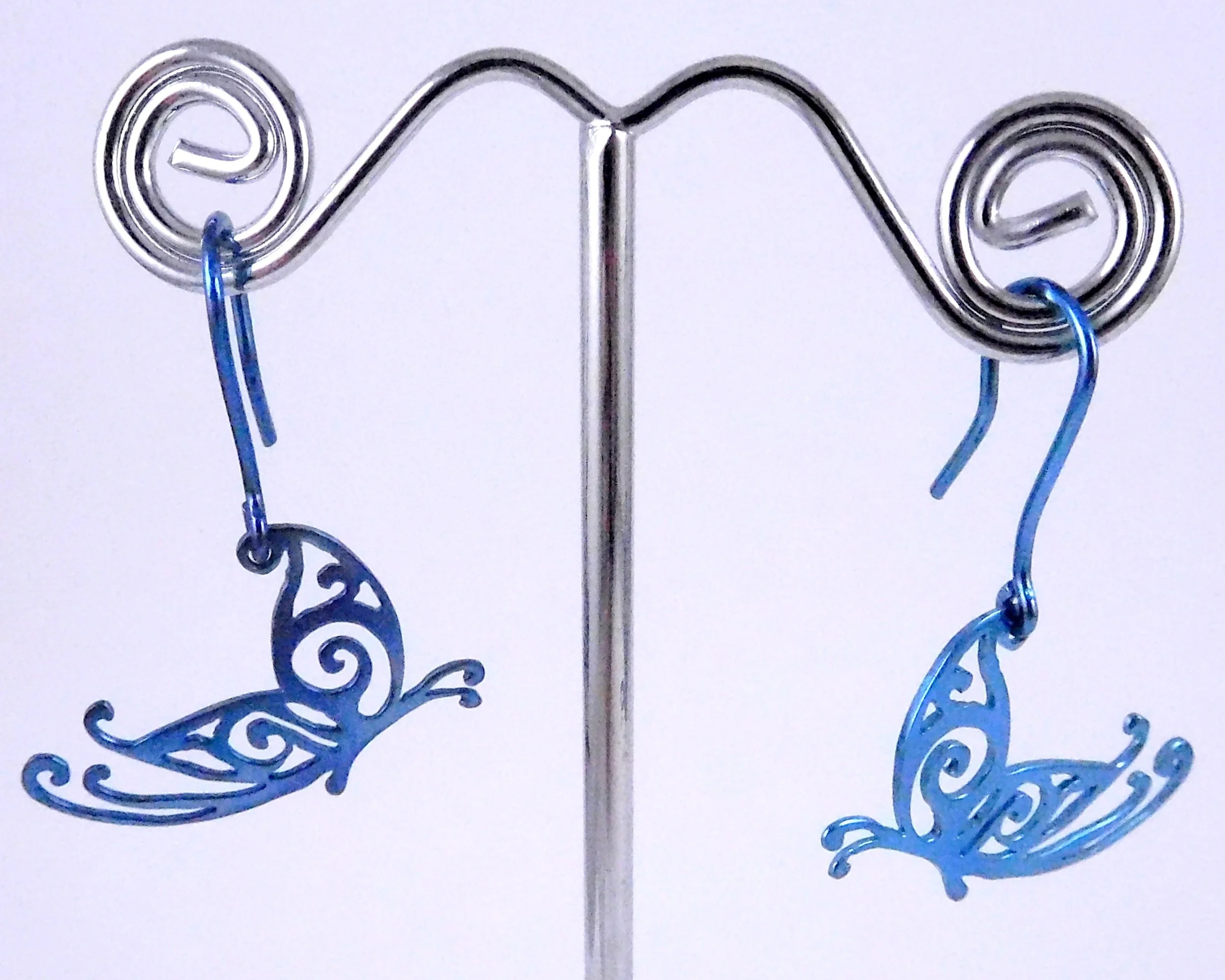 Metal wire earrings with blue swirling butterfly decorative elements hanging from earlobe hooks.