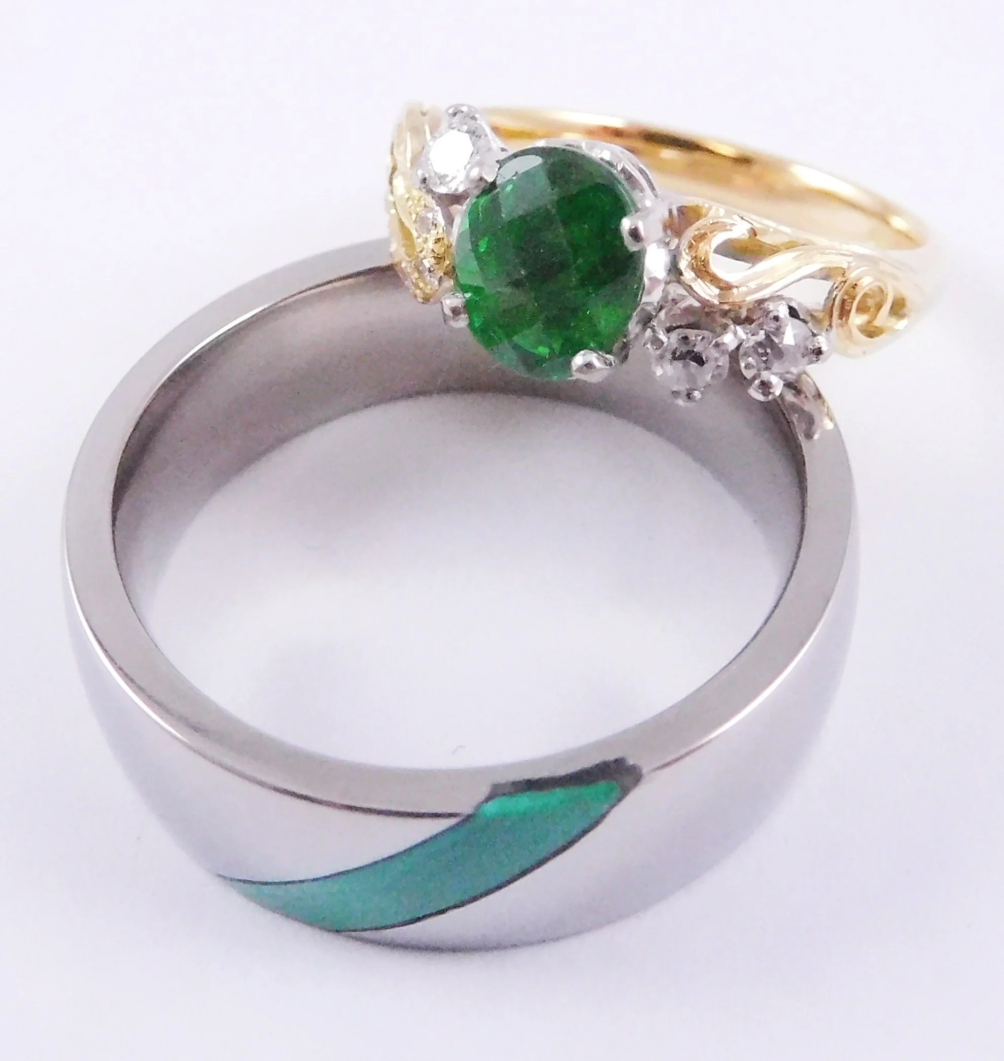 Close-up of a ring with a large, round, green tsavorite garnet gemstone and small surrounding diamonds, set on a white gold band set with semi-precious gemstone.
