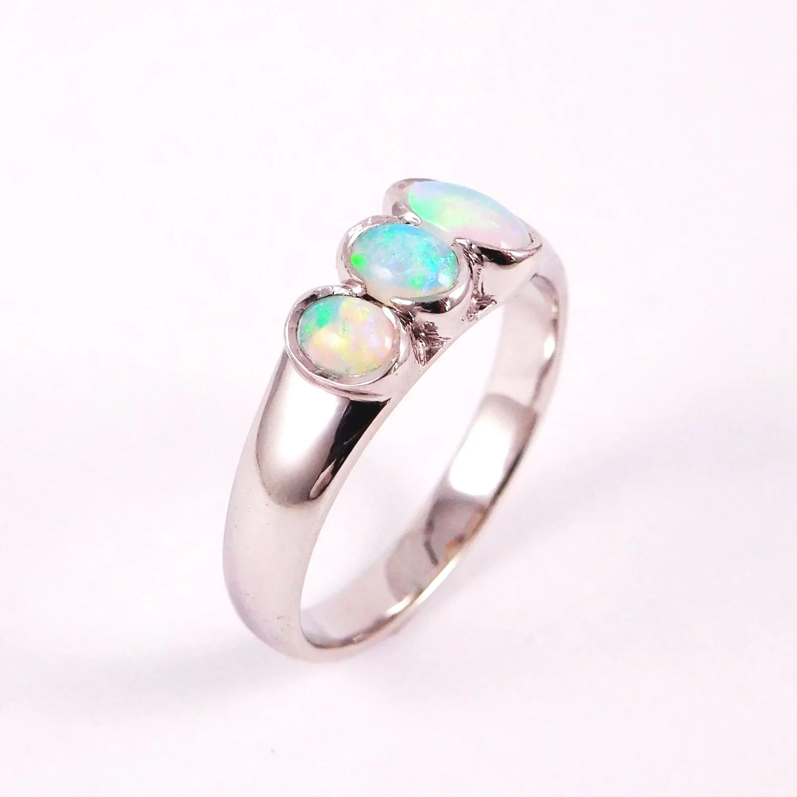 A silver ring with three opal gemstones set on top, displaying iridescent colors of blue, green, and pink.