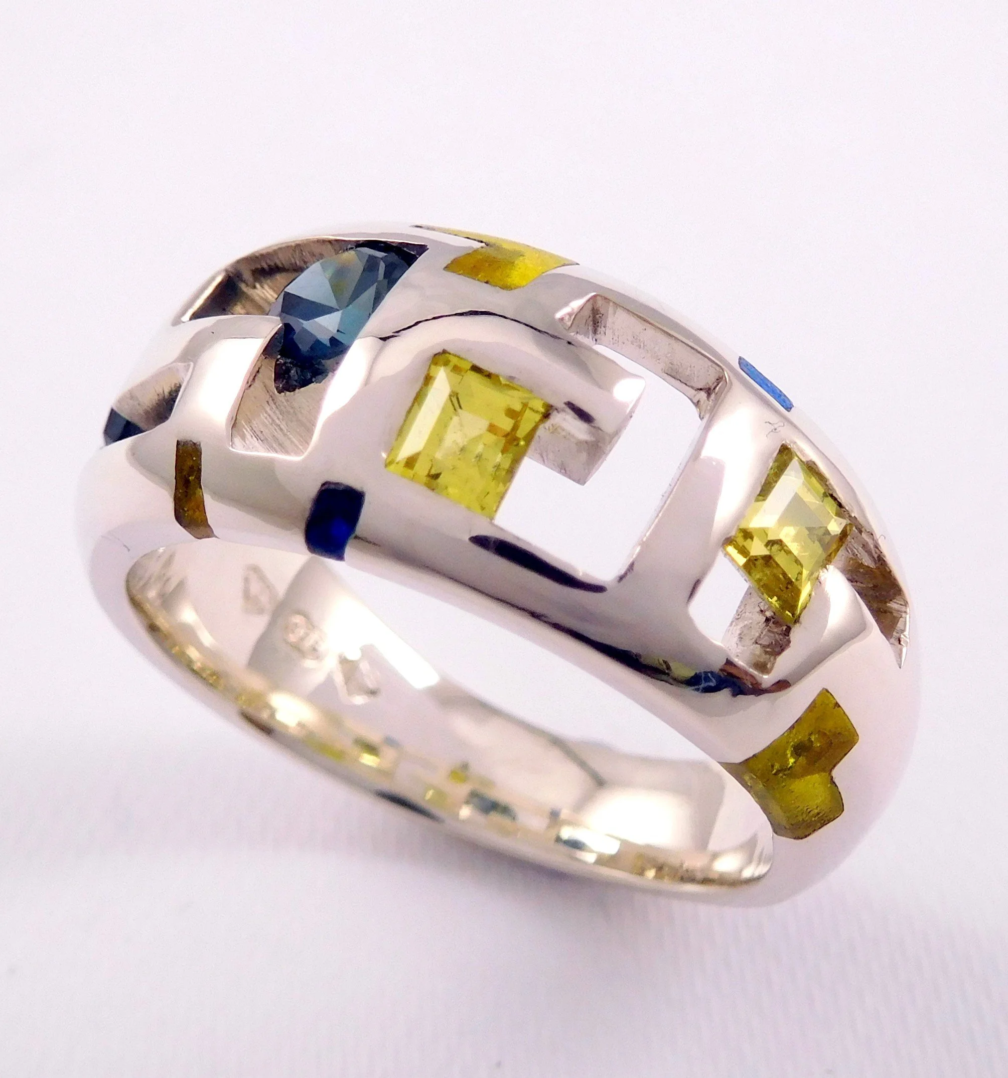 Close-up of a white gold ring with square yellow and blue gemstones on a white background.