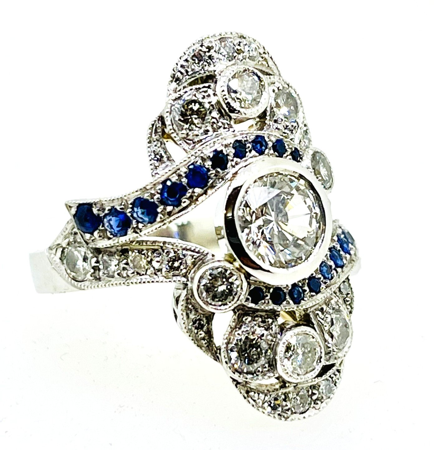 A silver ring with multiple embedded diamonds and blue sapphires, featuring an elaborate design with leaf and circular motifs.