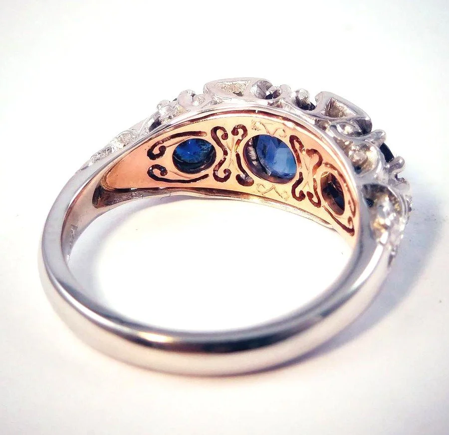 Close-up of a silver ring with blue gemstones and intricate gold and black detailing inside the band.