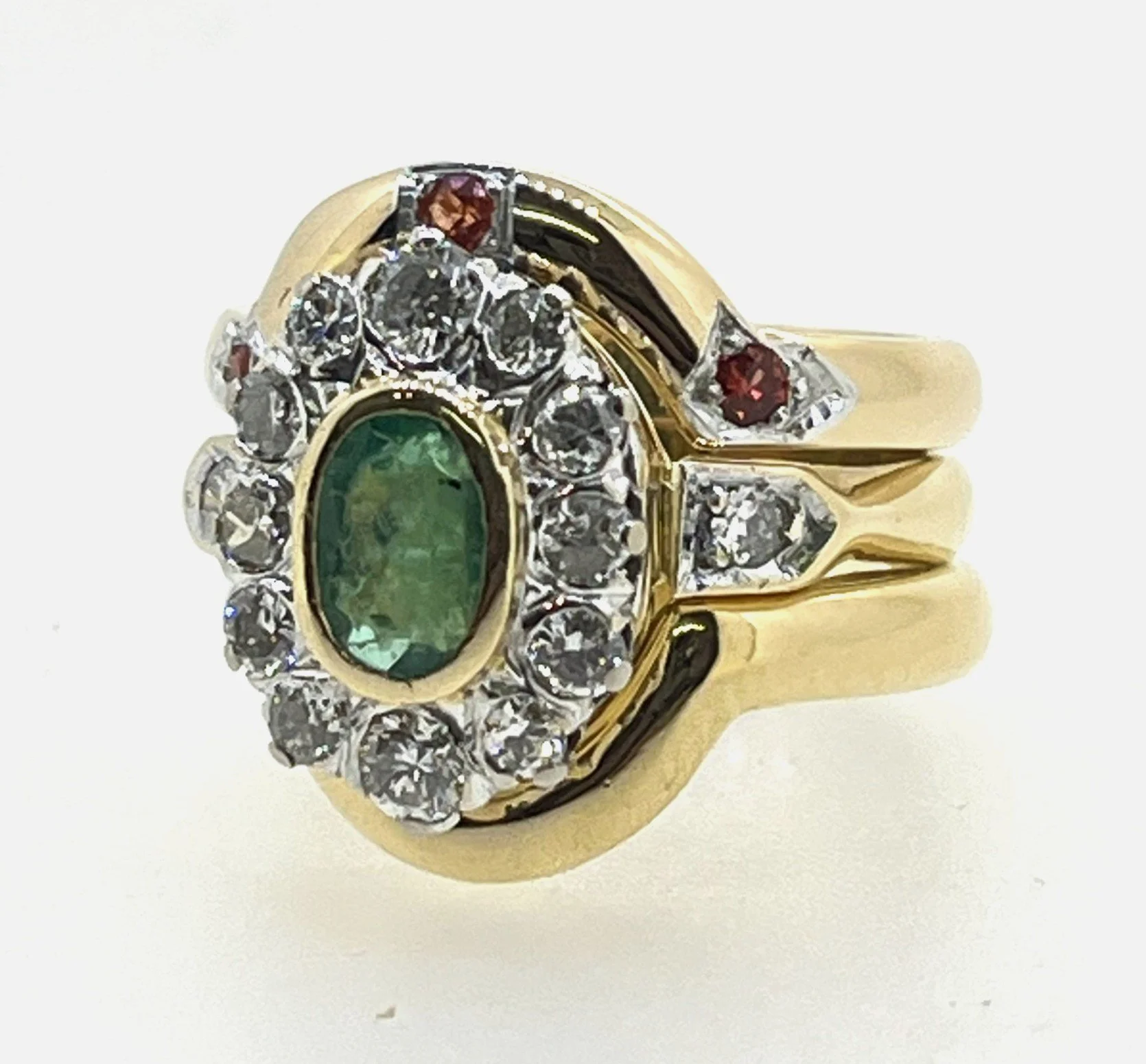 A gold ring with an oval green gemstone surrounded by clear diamonds and two small red stones on either side.