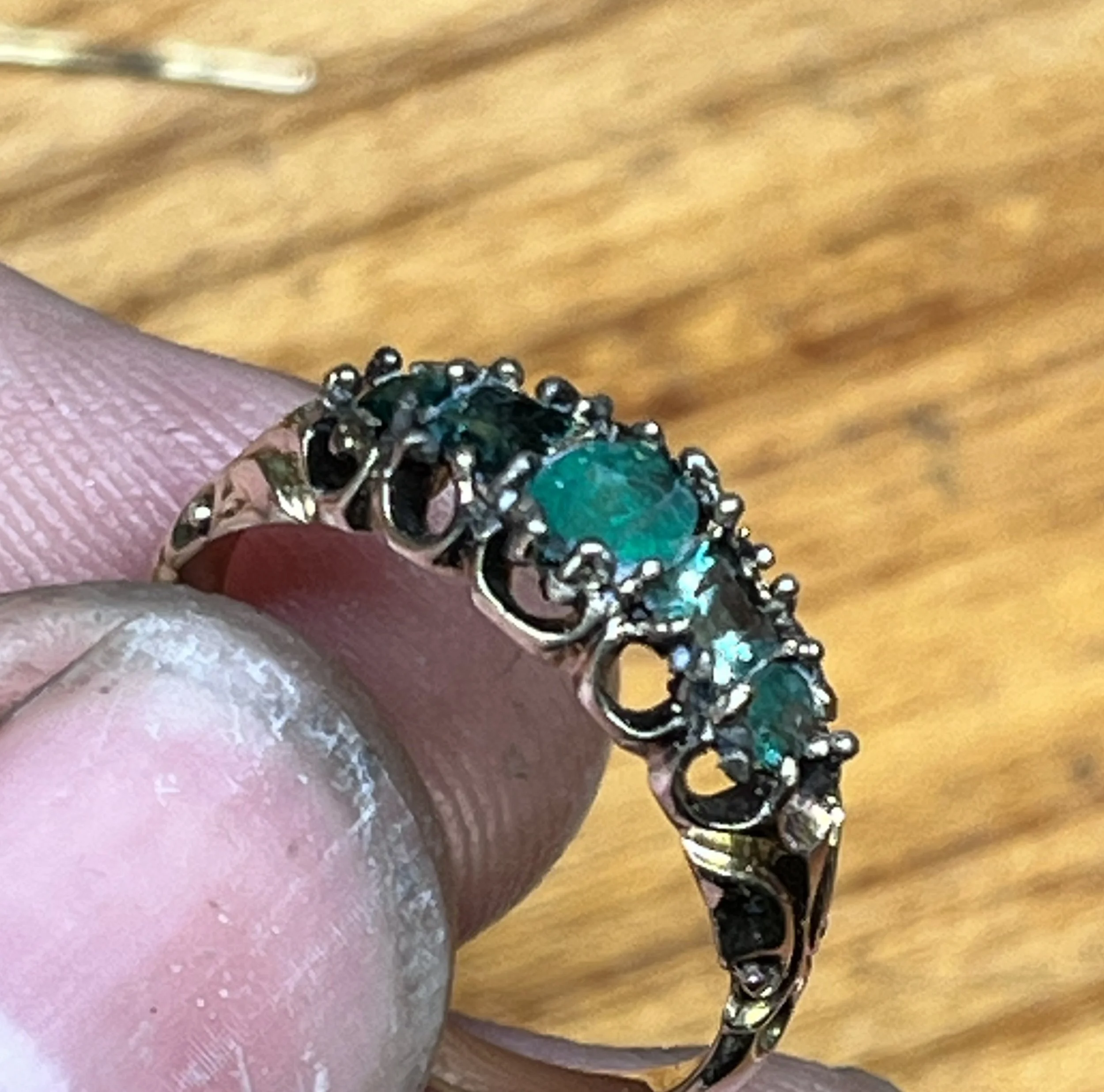 Close-up of a person's hand wearing a large ornate ring with emerald stones.