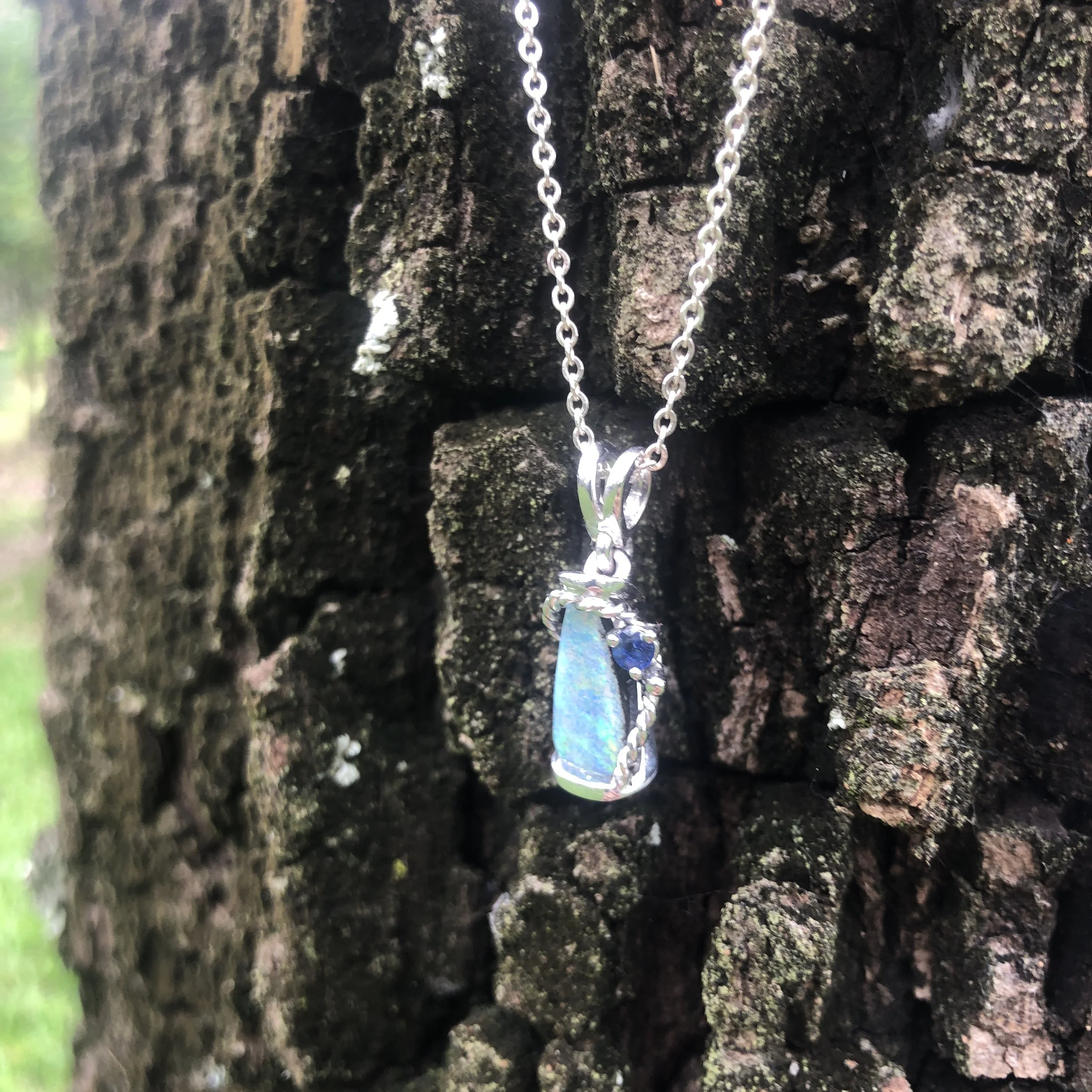 Opal pendant hanging against a rough, textured rock wall outdoors.