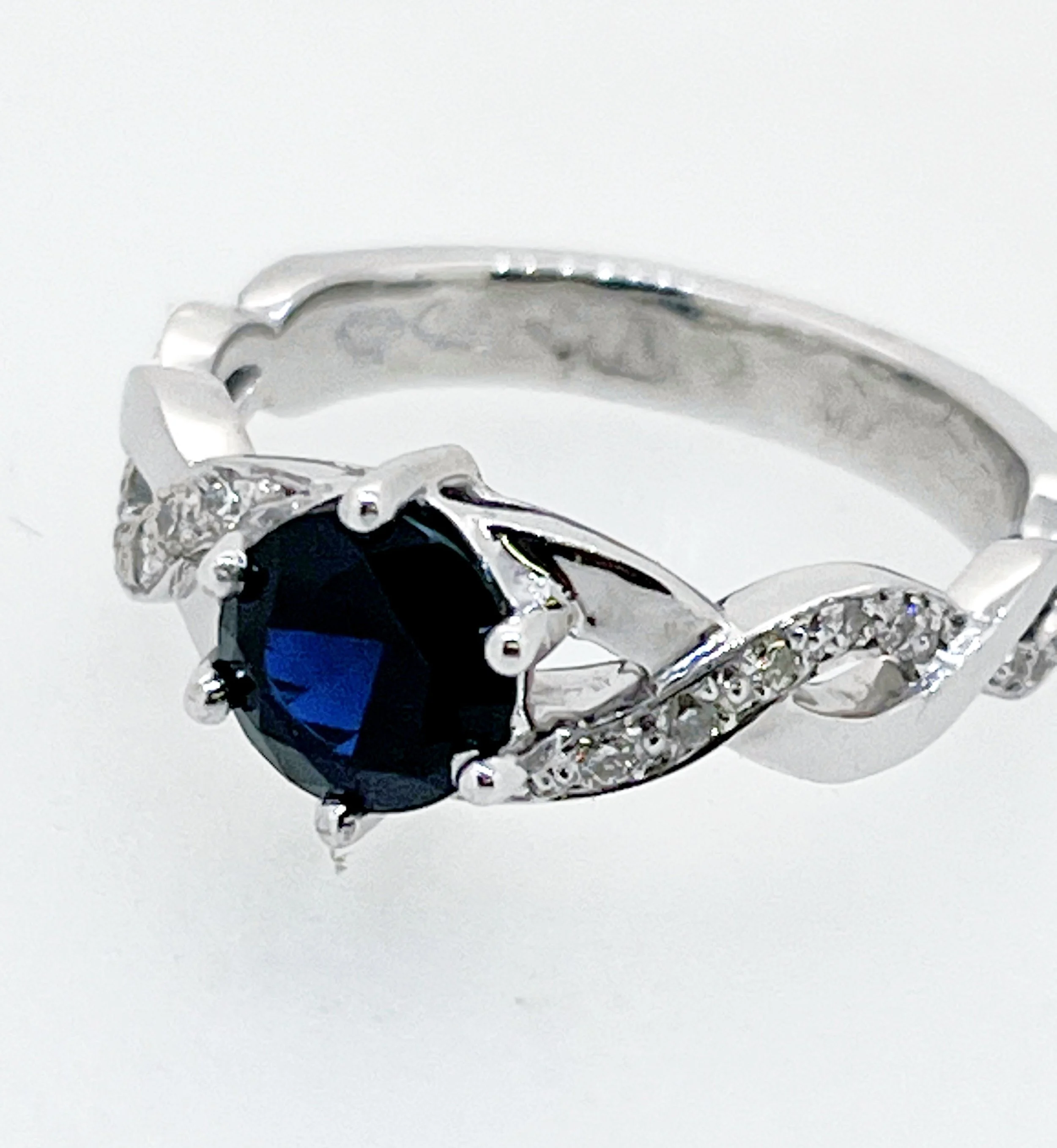 Close-up of a silver ring with a dark blue gemstone and intricate decorative details on a white background.