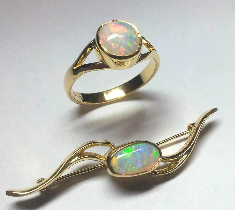 A gold ring and a gold pin, each with a luminous opal gemstone, on a white surface.