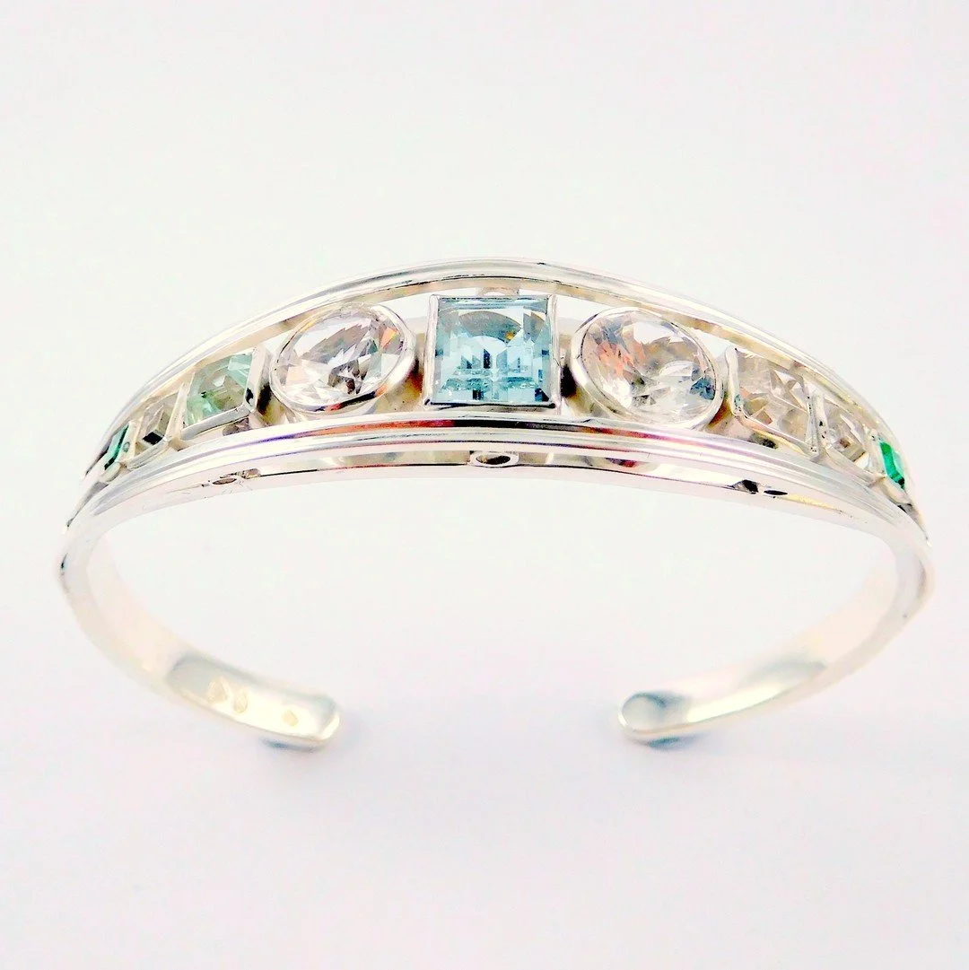 Silver bangle with multiple embedded gemstones of various shapes and colours