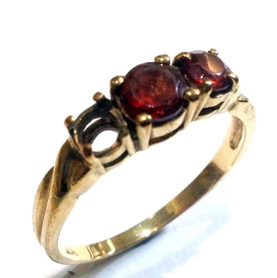 A gold ring with two oval red gemstones and intricate detailing.