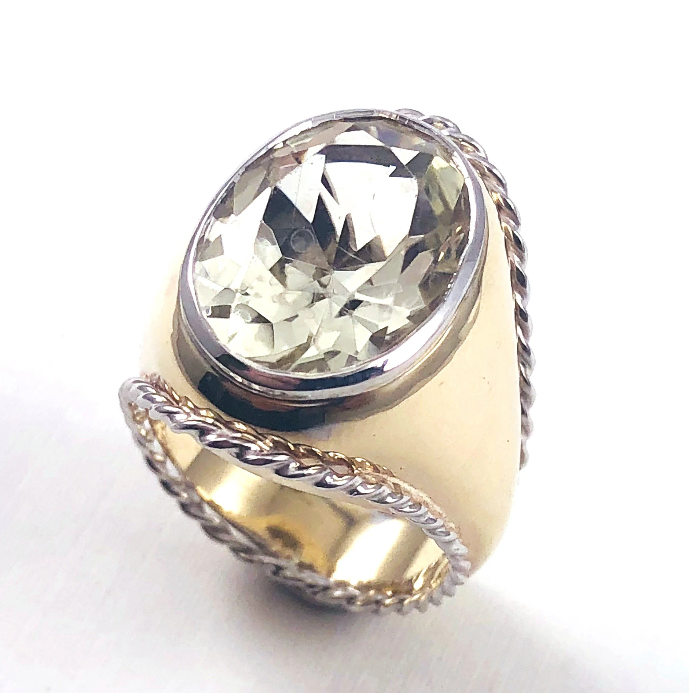 Close-up of a diamond ring with detailed band design on a white surface.