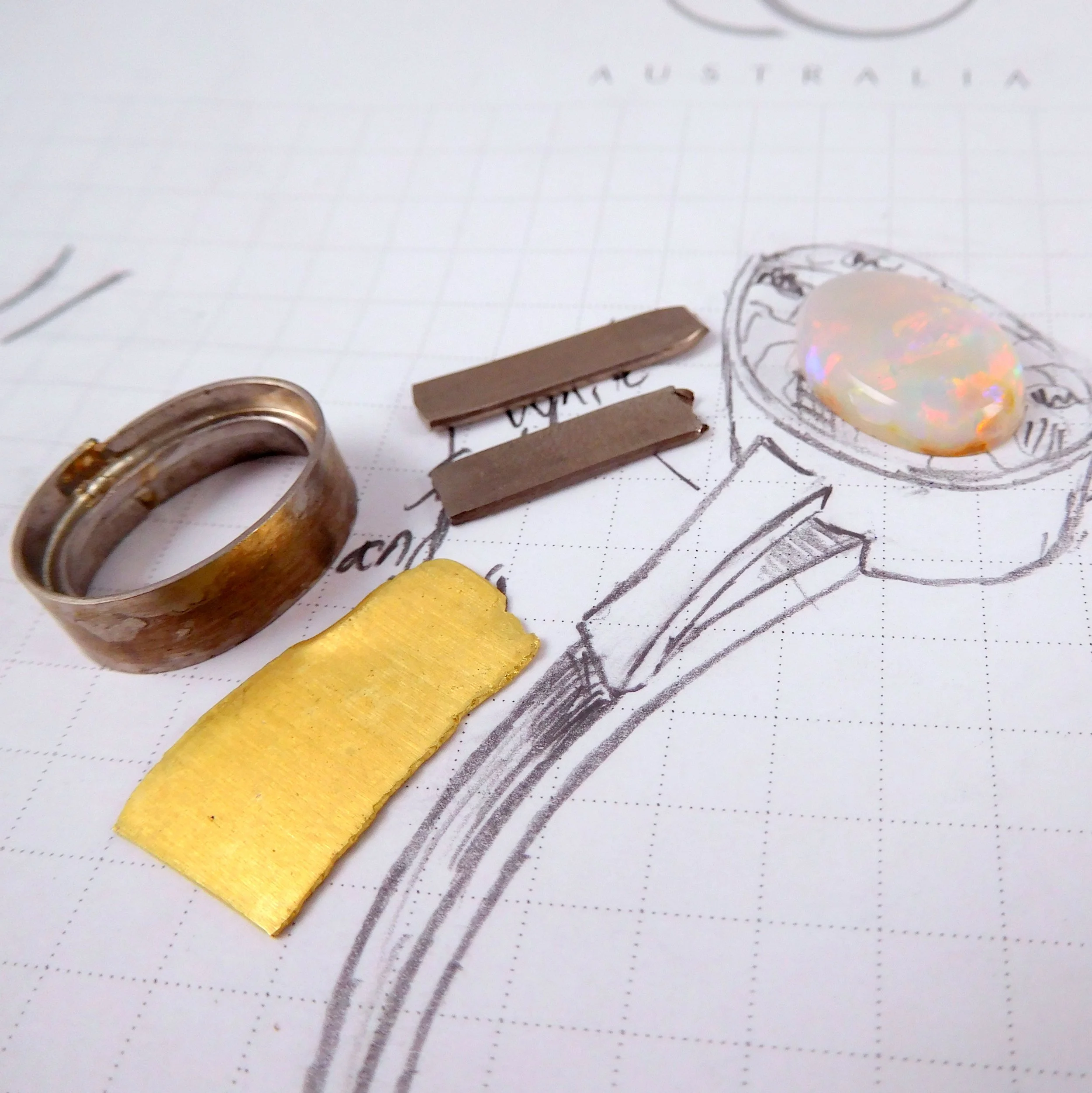Some raw ring materials (metals and stone) overtop a drawing.