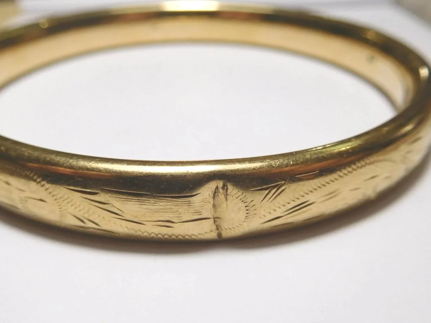 Close-up of a dent on a gold bangle with intricate engraved patterns.