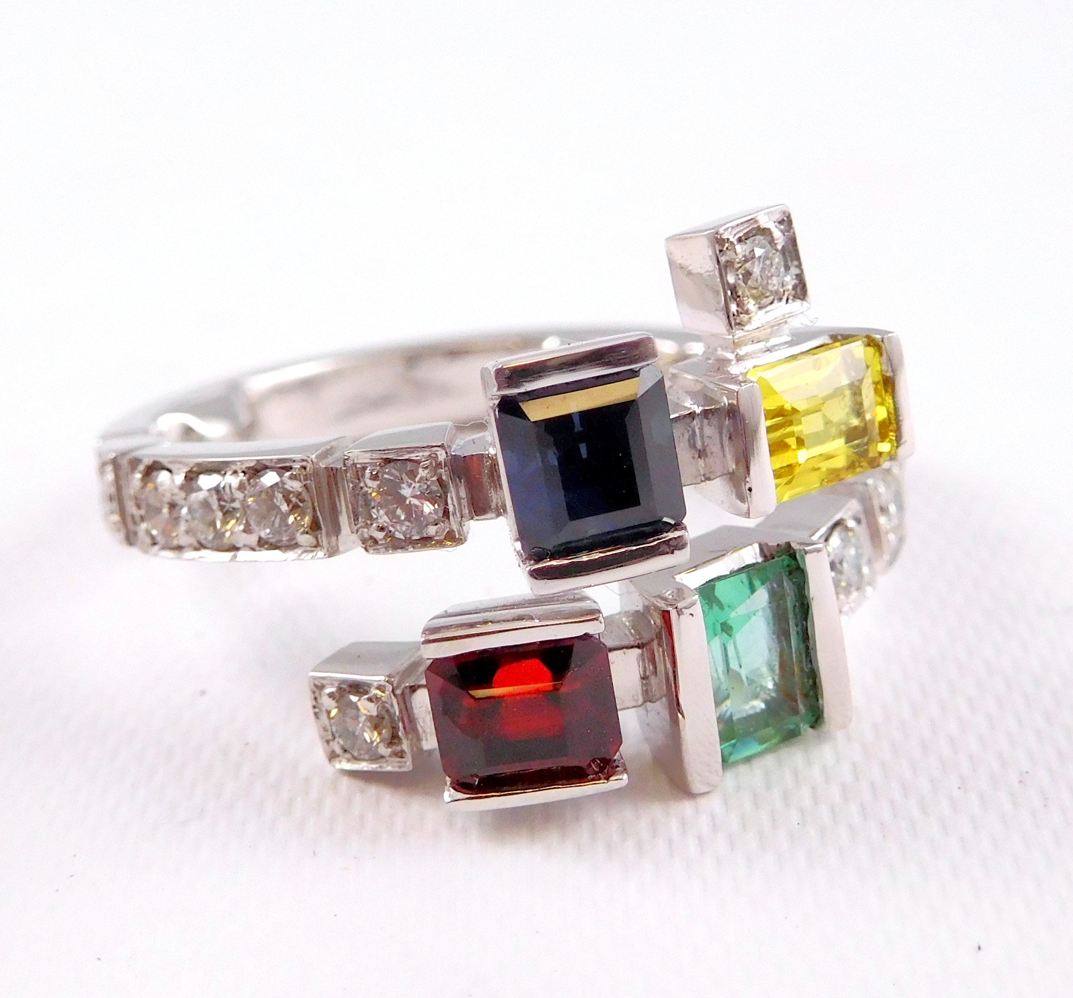 An "arty" white gold ring featuring square-cut gemstones in different colors, including yellow, black, red, green, and diamonds. 