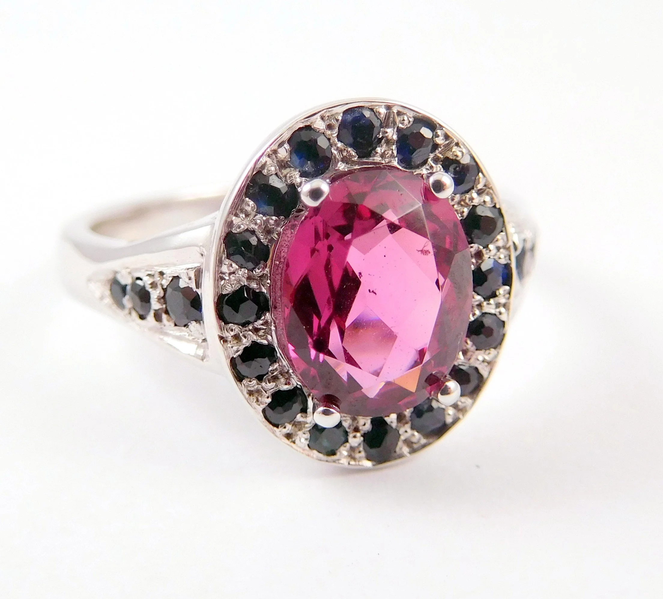 Close-up of a silver ring with a large pink gemstone and smaller black and clear stones surrounding it.
