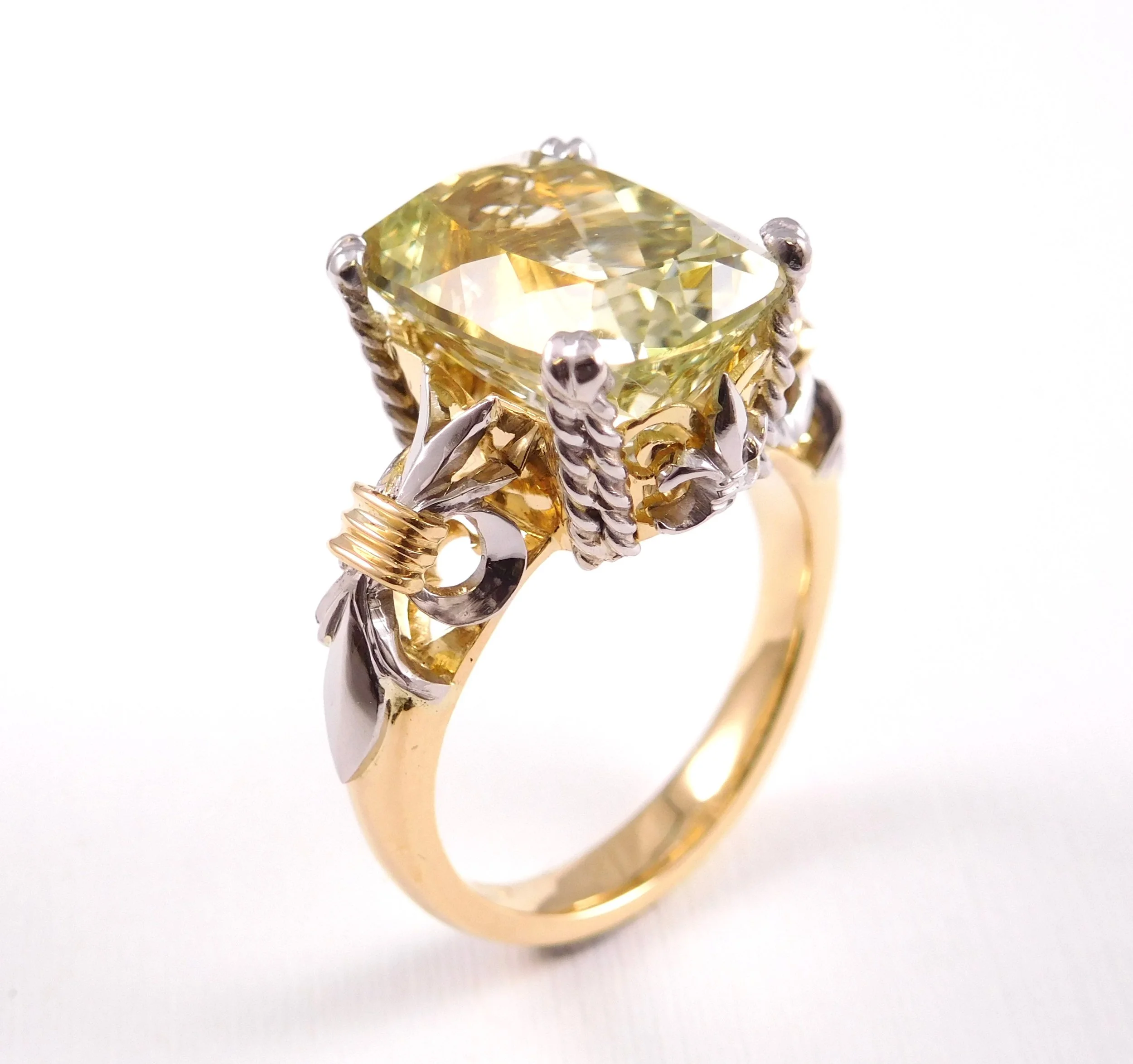 Close-up of a gold and silver ring with a large, cushion-cut yellow diamond in a prong setting.