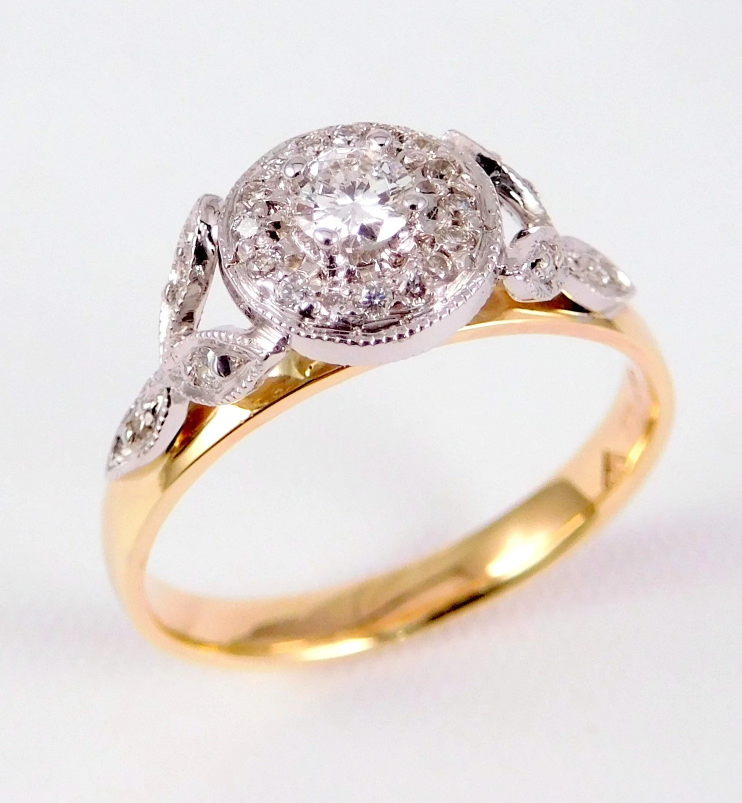 A gold and silver ring with a large central diamond surrounded by smaller diamonds, featuring intricate silver detailing on the band.