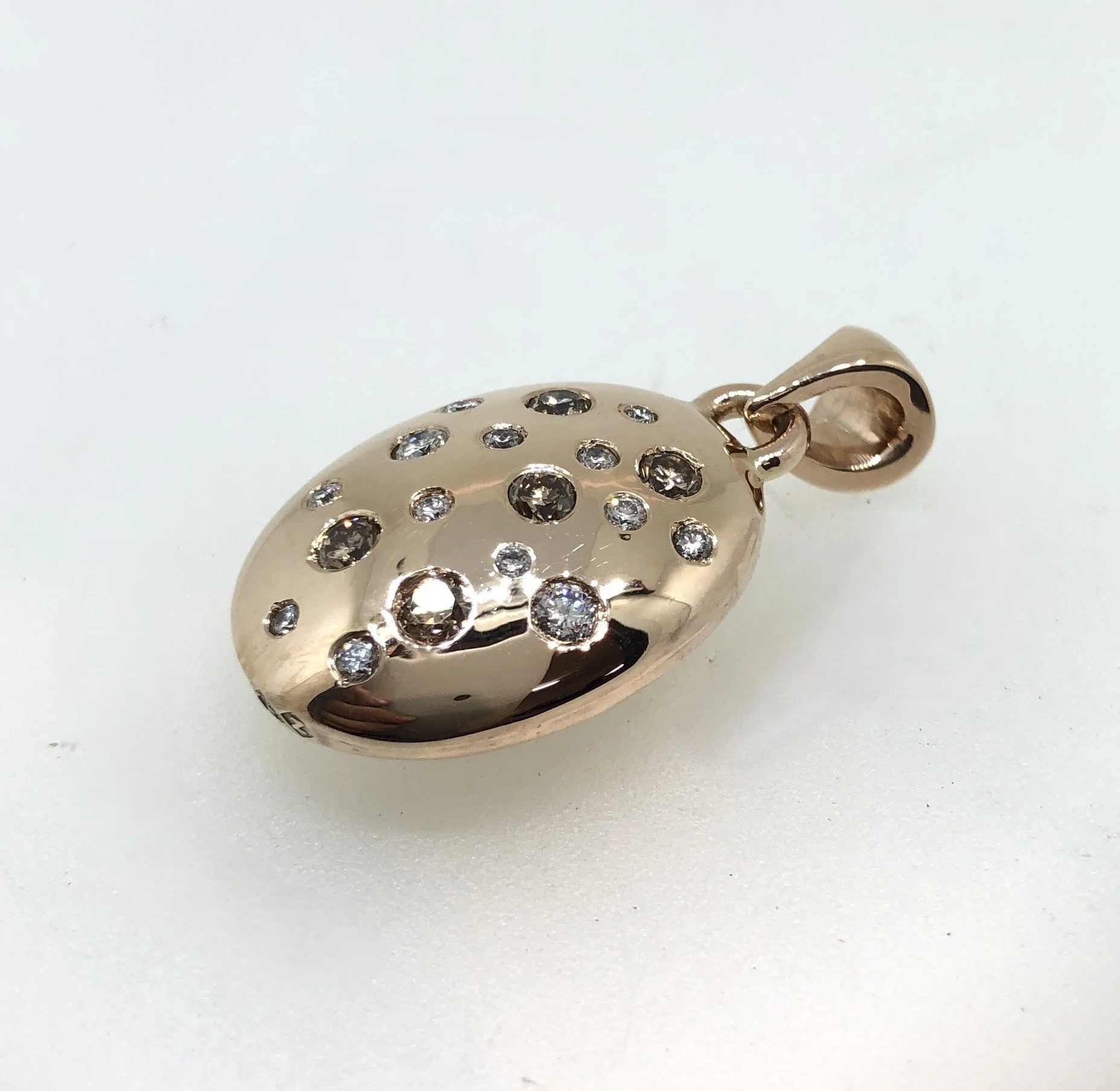 Close-up of an oval gold pendant, adorned with numerous small, sparkling diamonds. 