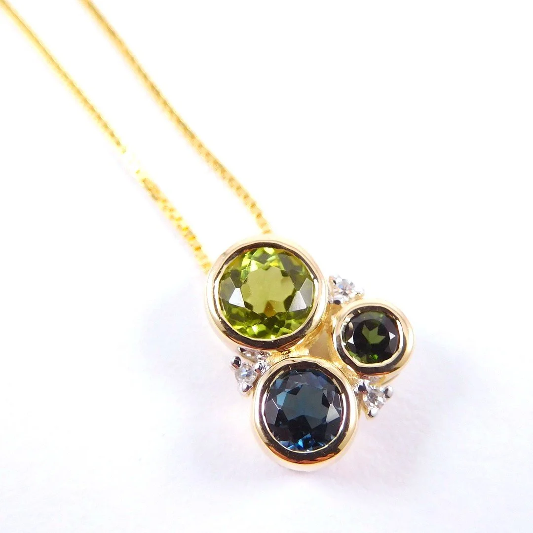 Gold necklace with three round gemstones in green, dark blue, and black, accented by small diamonds.