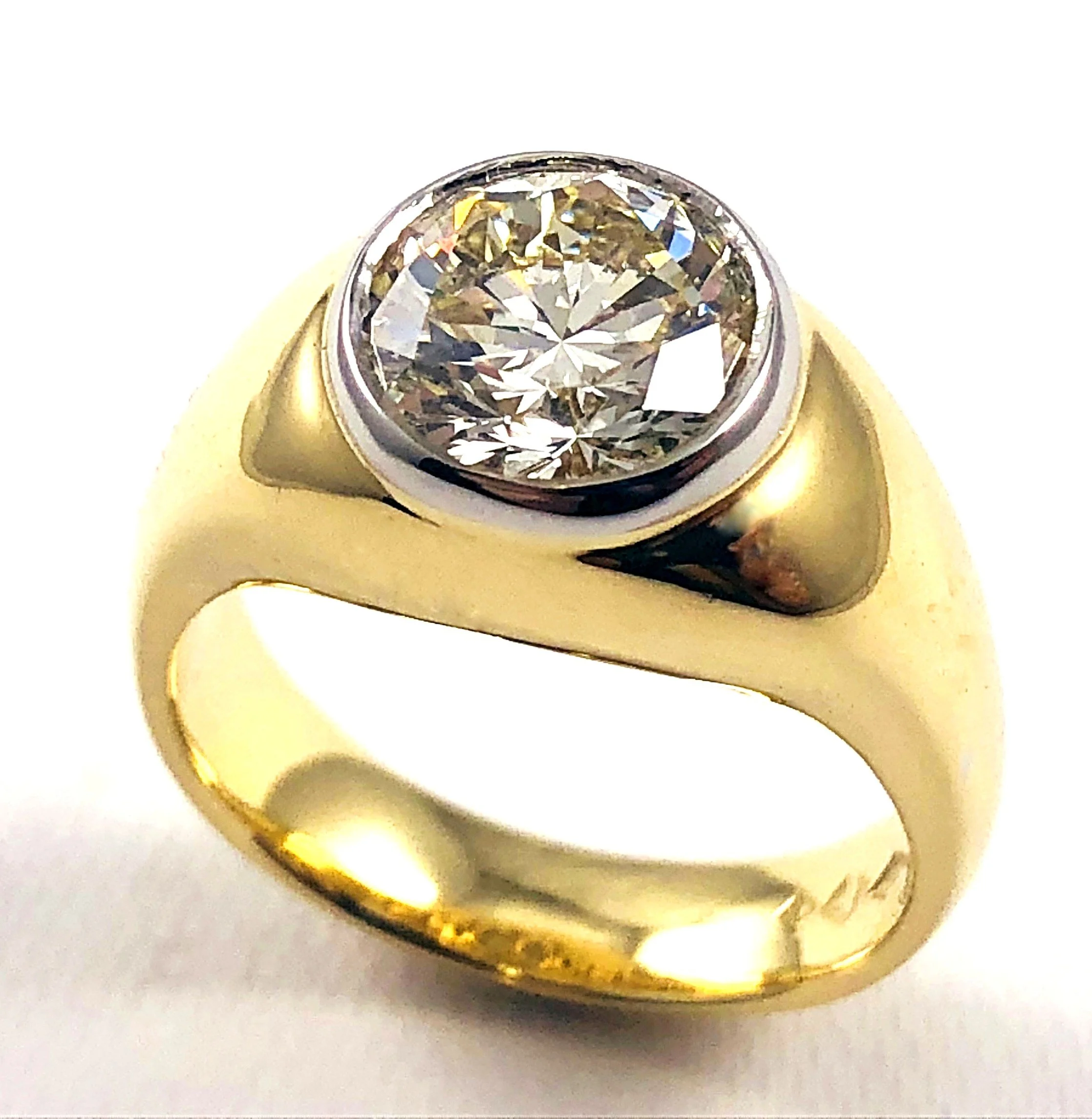A close-up image of a gold ring with a large, brilliant-cut diamond solitaire. The diamond is round and sparkly, set in a bezel setting on a shiny gold band.