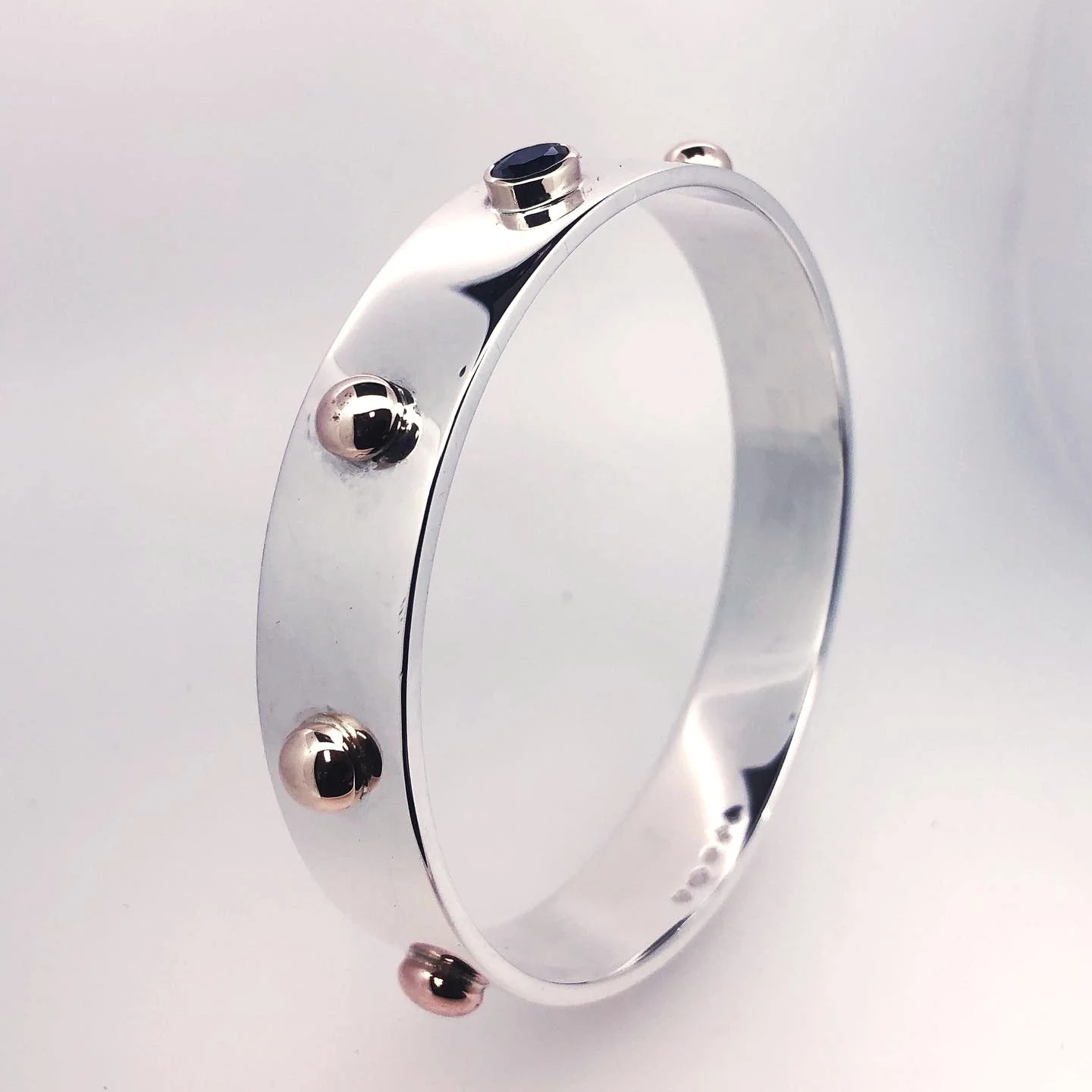 A silver bracelet with a smooth surface and small round studs, some with black details