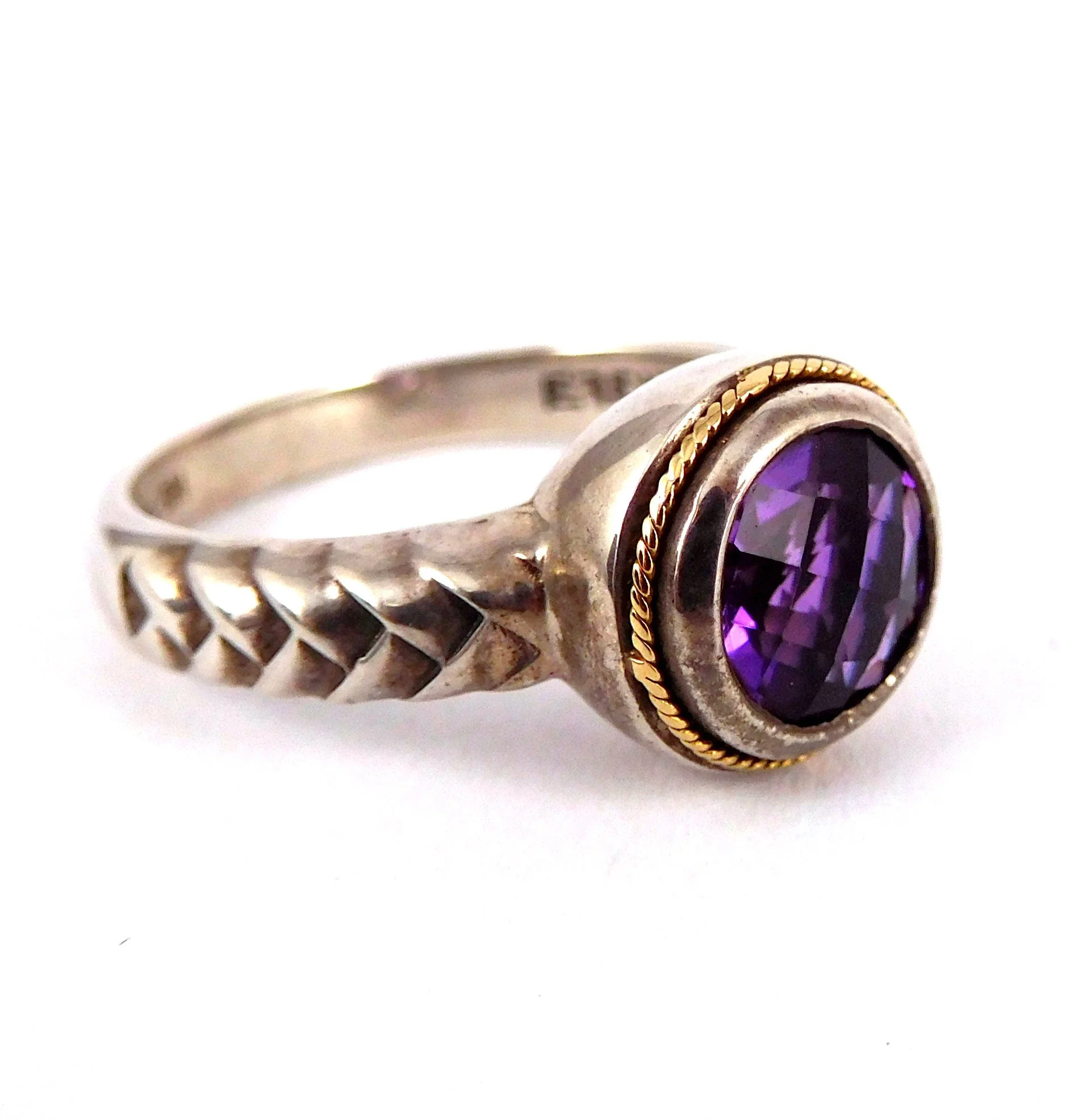Close-up of a silver ring with a large purple amethyst gemstone and decorative gold detailing around the stone.