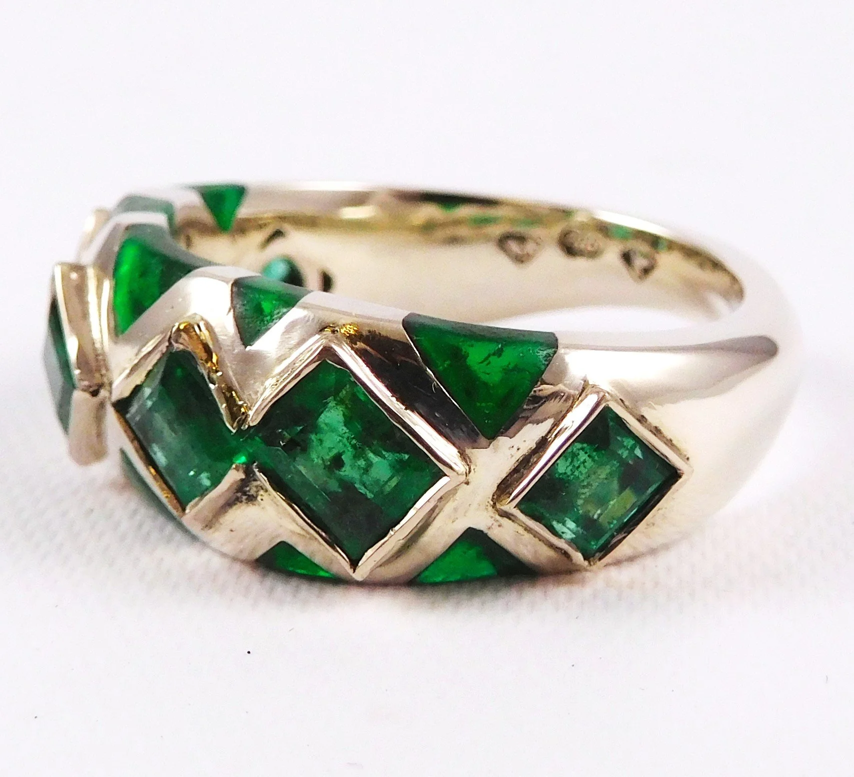 Close-up of a ring with a white gold band and green emerald gemstones arranged in a zigzag pattern