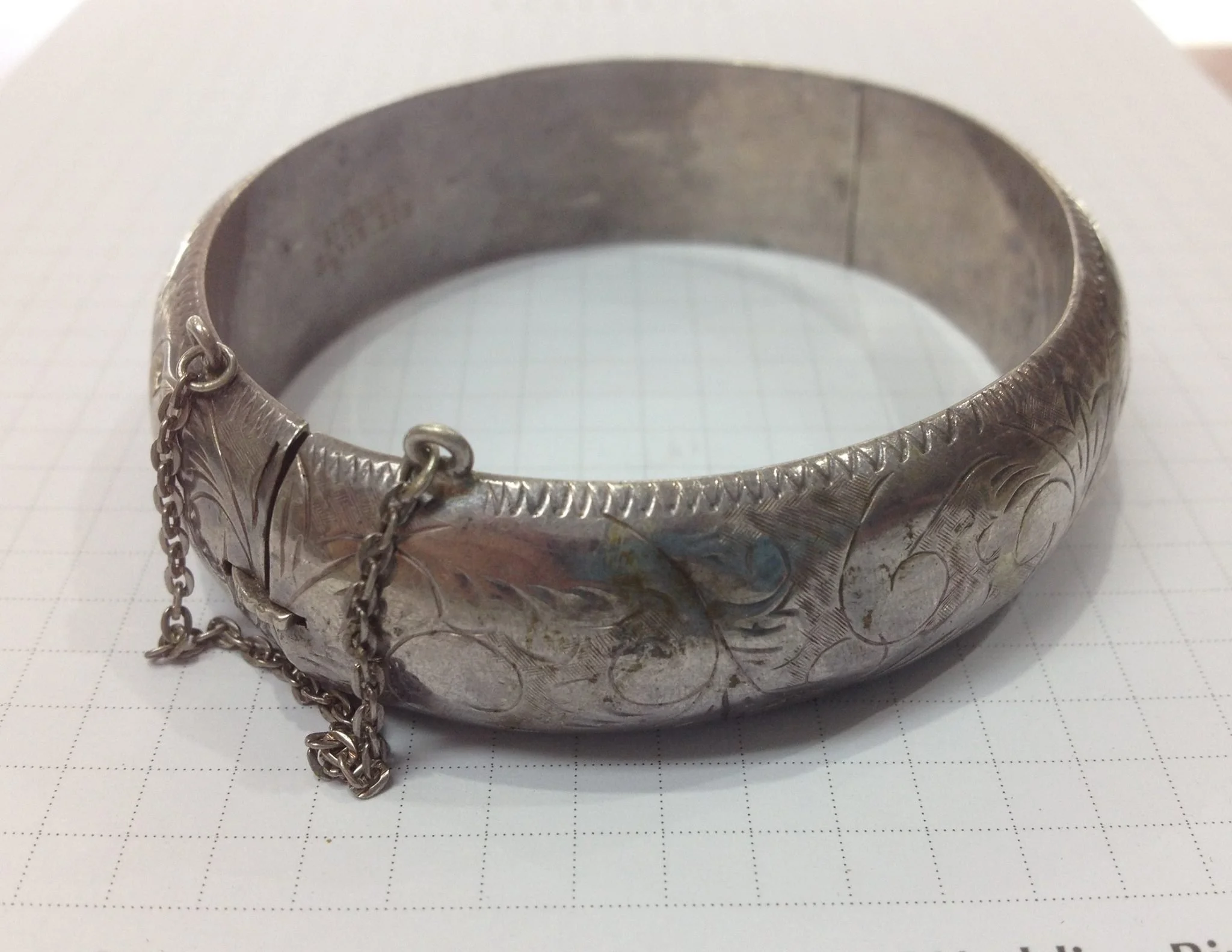 Close-up of a decorative silver bracelet with intricate engraved patterns and attached chains.