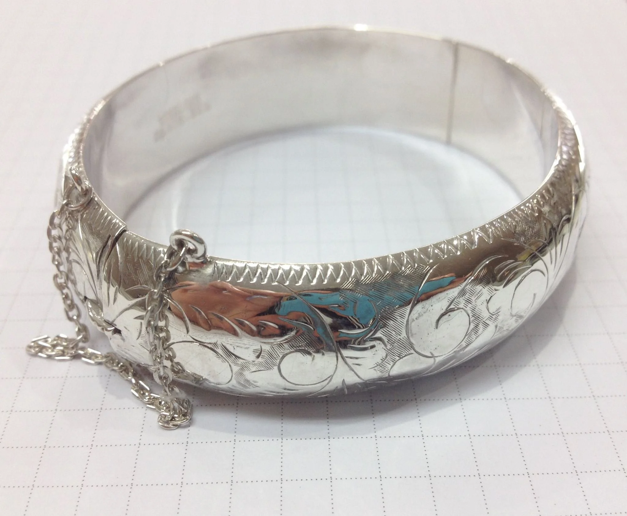 Silver bangle with ornate engraved and chain details.