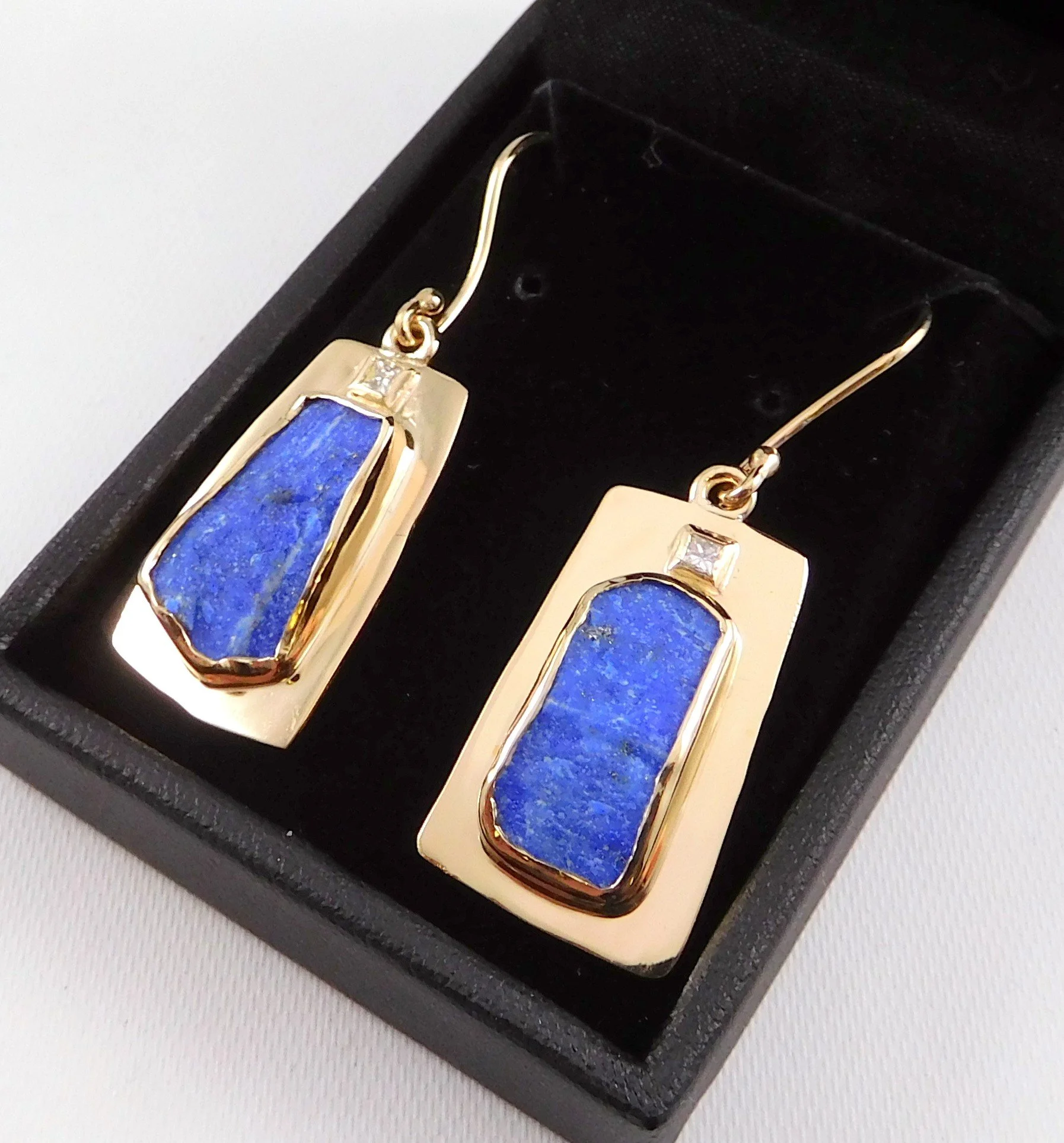 Close-up of gold earrings with blue turquoise stones placed in a black jewelry box.