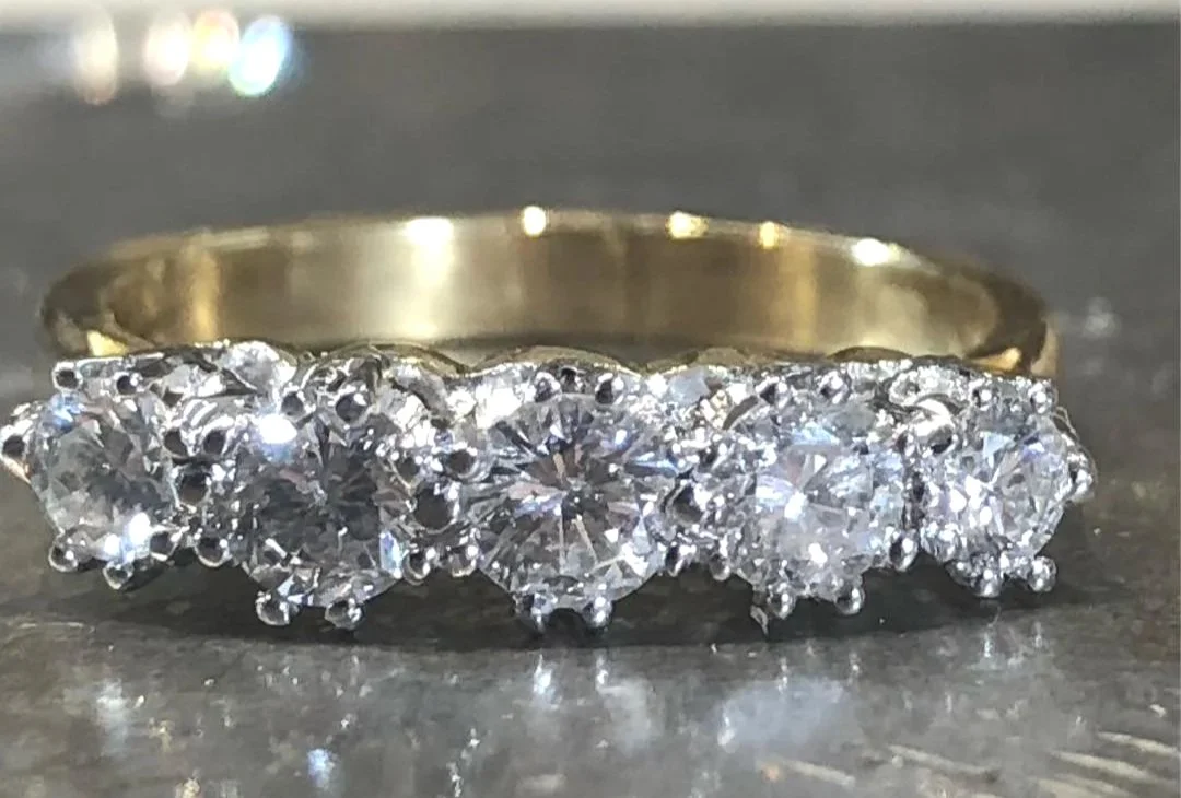 A gold ring with nine large diamonds arranged in a row on top of a dark surface.