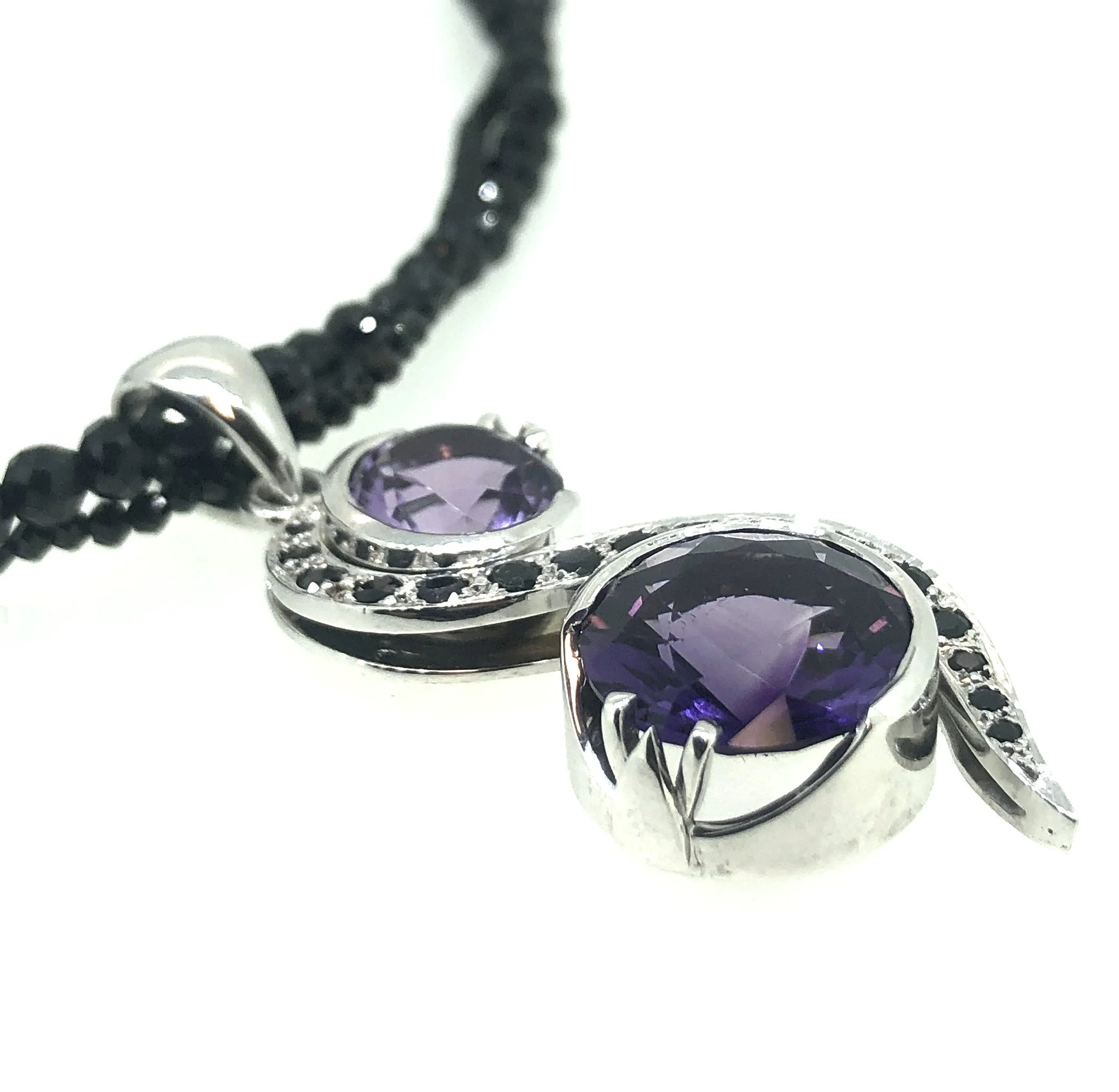 Close-up of a piece of jewelry with dark purple gemstones and silver setting, along with a black gemstone beaded chain.