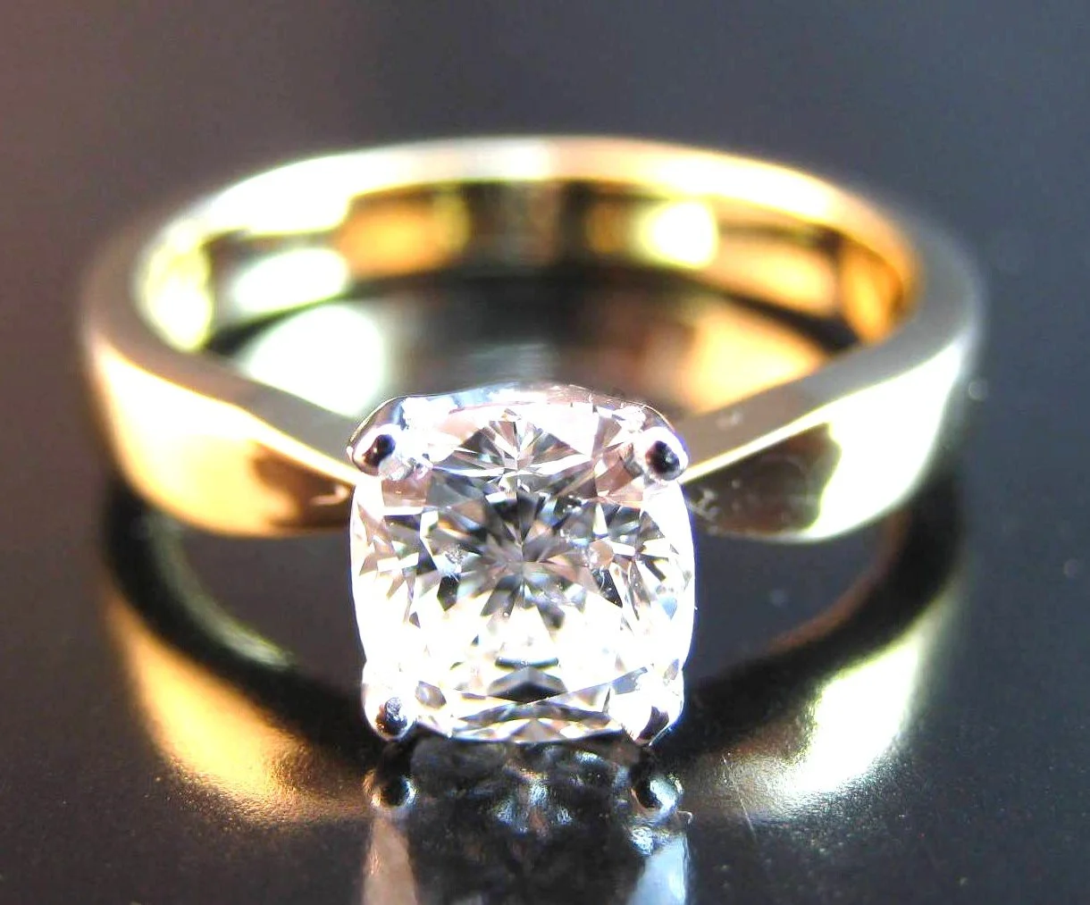 Close-up of a gold ring with a large, sparkling diamond on a reflective dark surface.