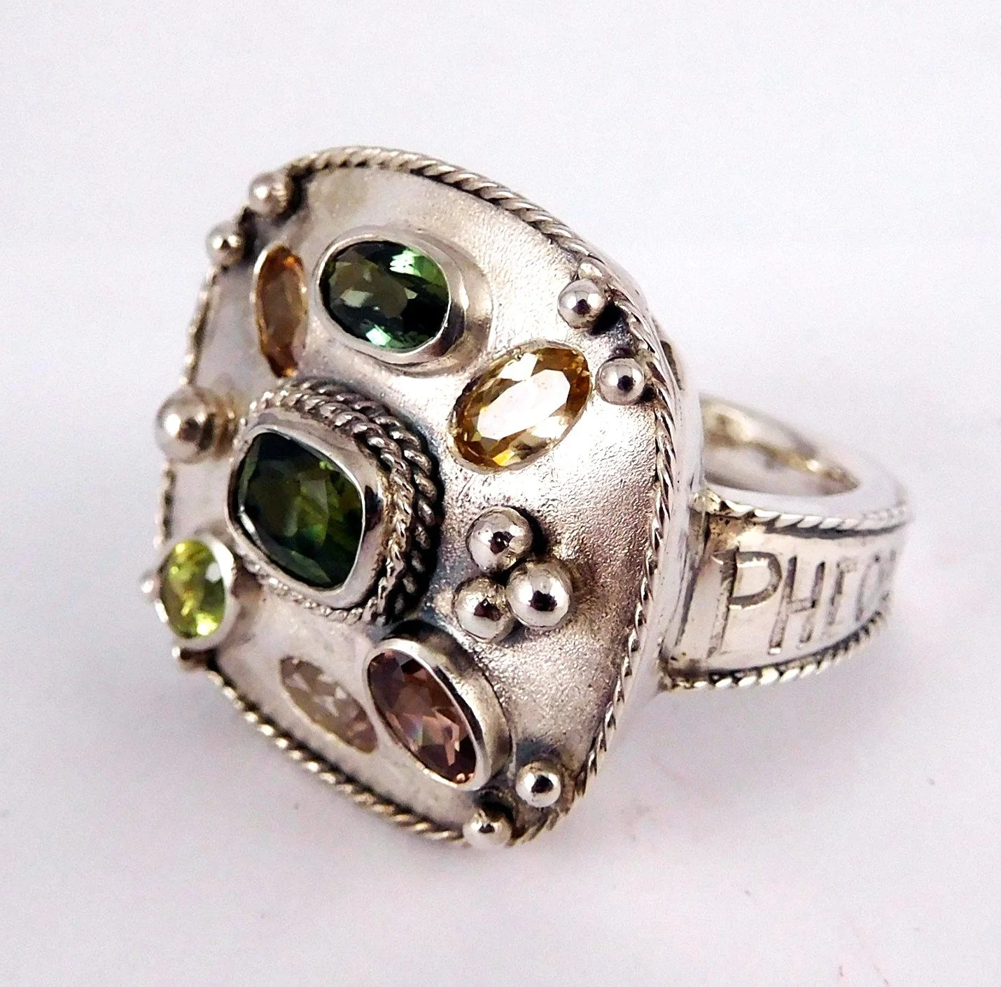A silver ring with various colored gemstones and decorative elements.