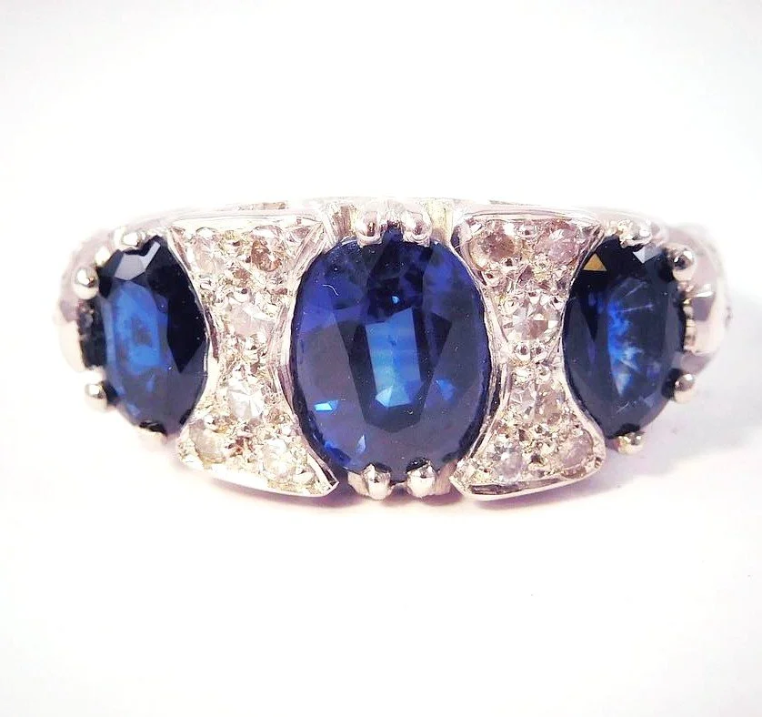 Ring with three large oval blue sapphires and smaller diamonds set in a silver or white gold band.