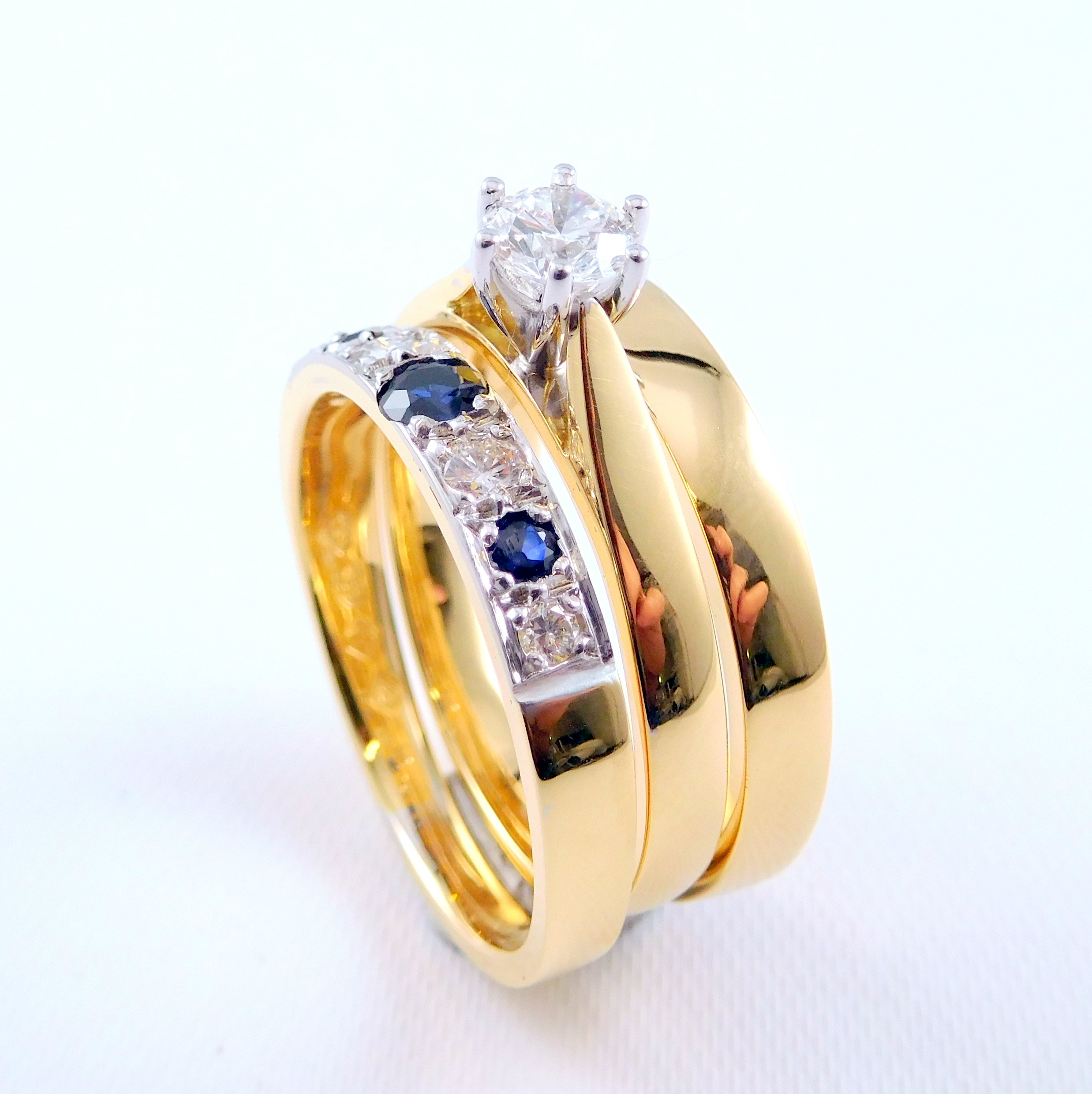 Close-up of a wedding and engagement rings each with a different gemstone, stacked together.